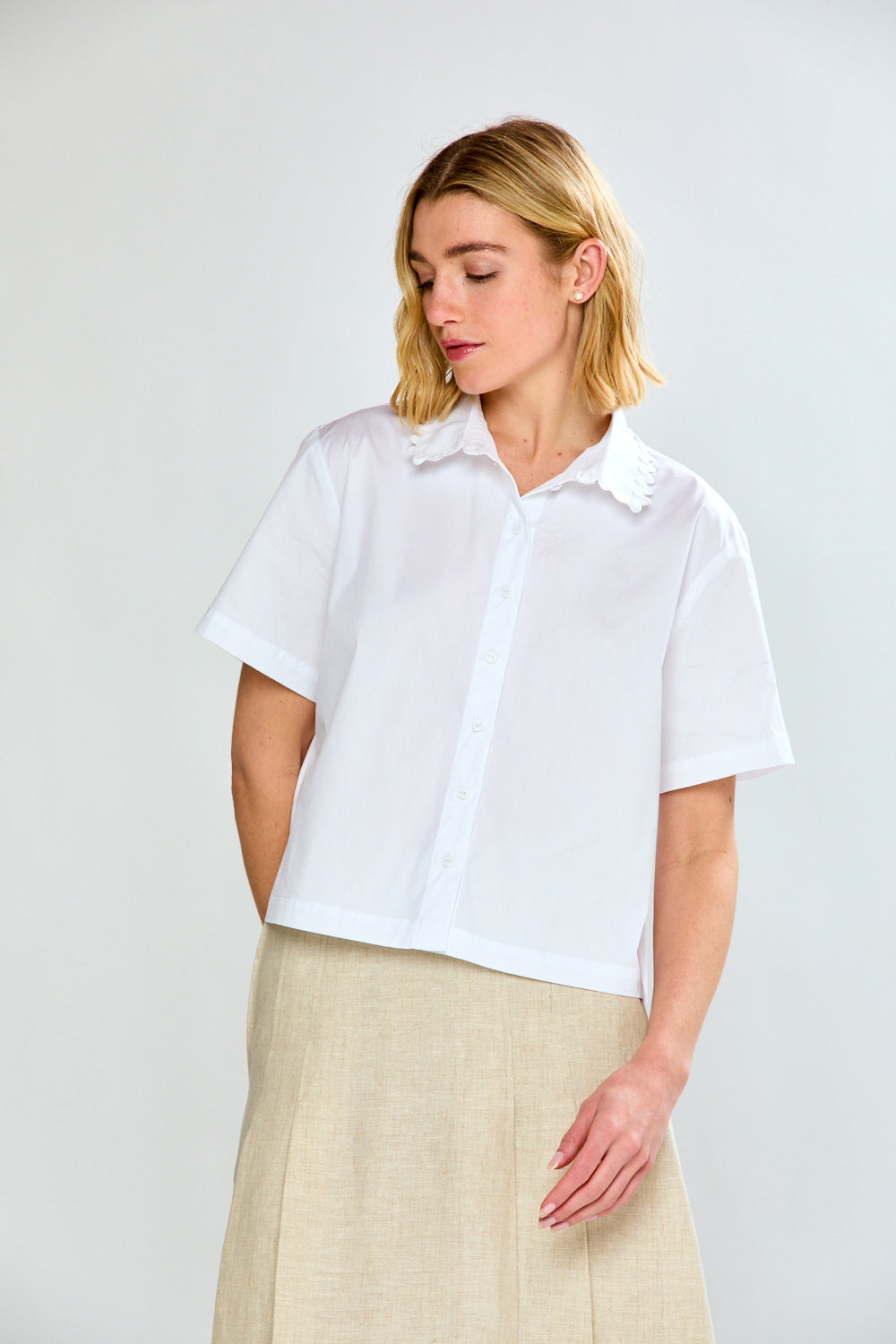 Woman wearing a white short-sleeve shirt and beige pants on a light gray background