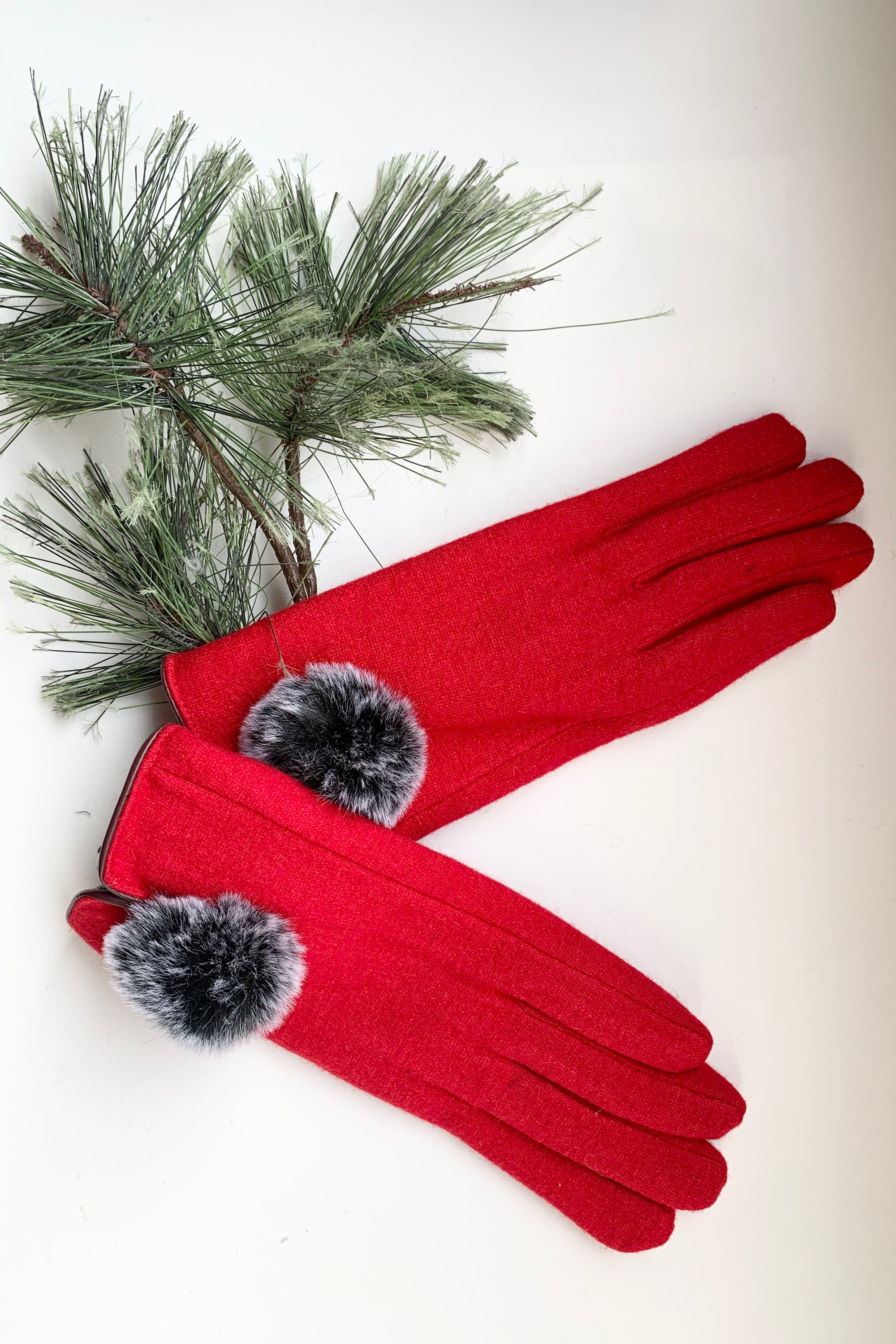Red gloves with black pom-poms on a white background with greenery.