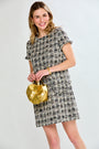Woman wearing a patterned dress holding a gold handbag against a white background