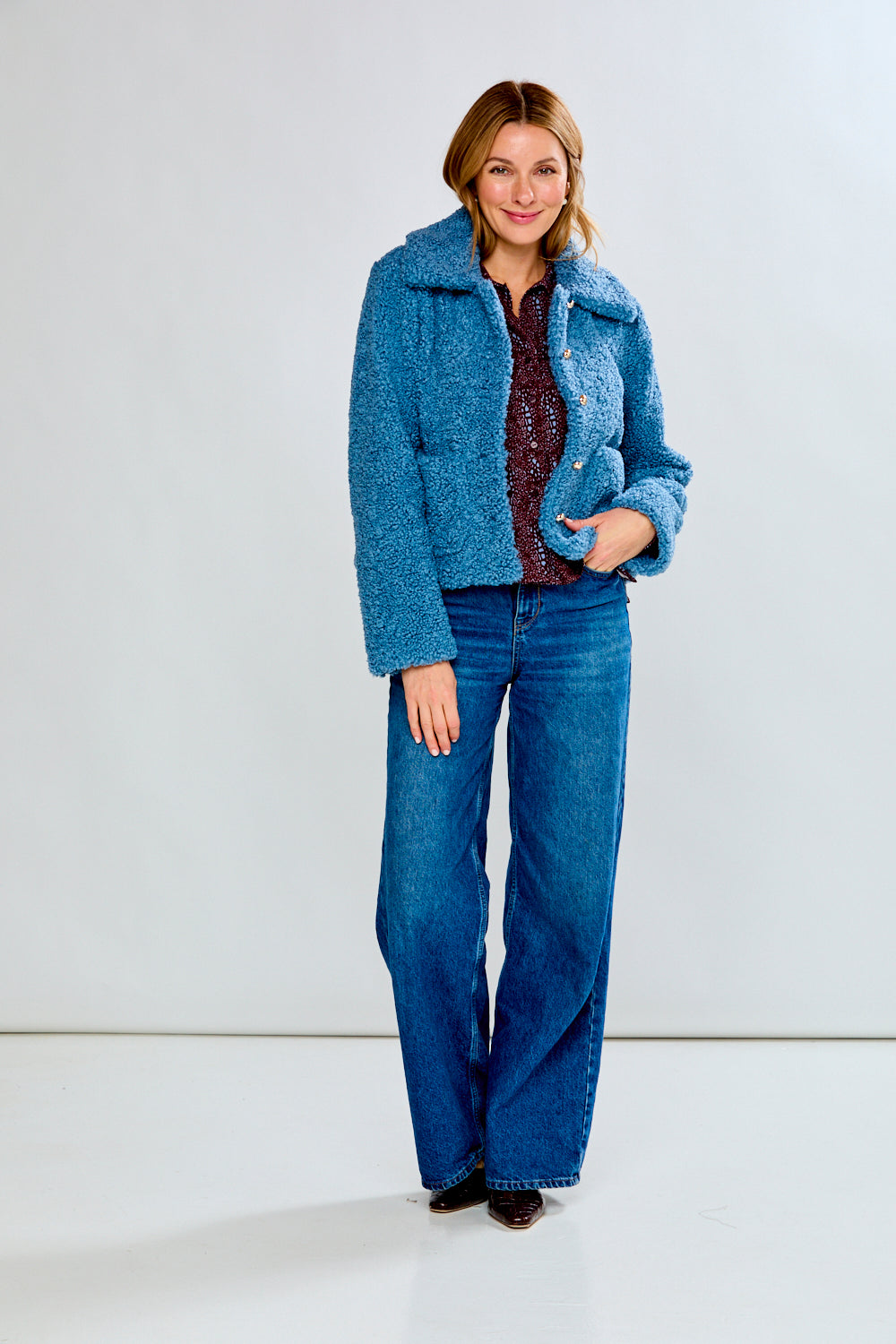 Woman wearing a blue coat and jeans against a white background