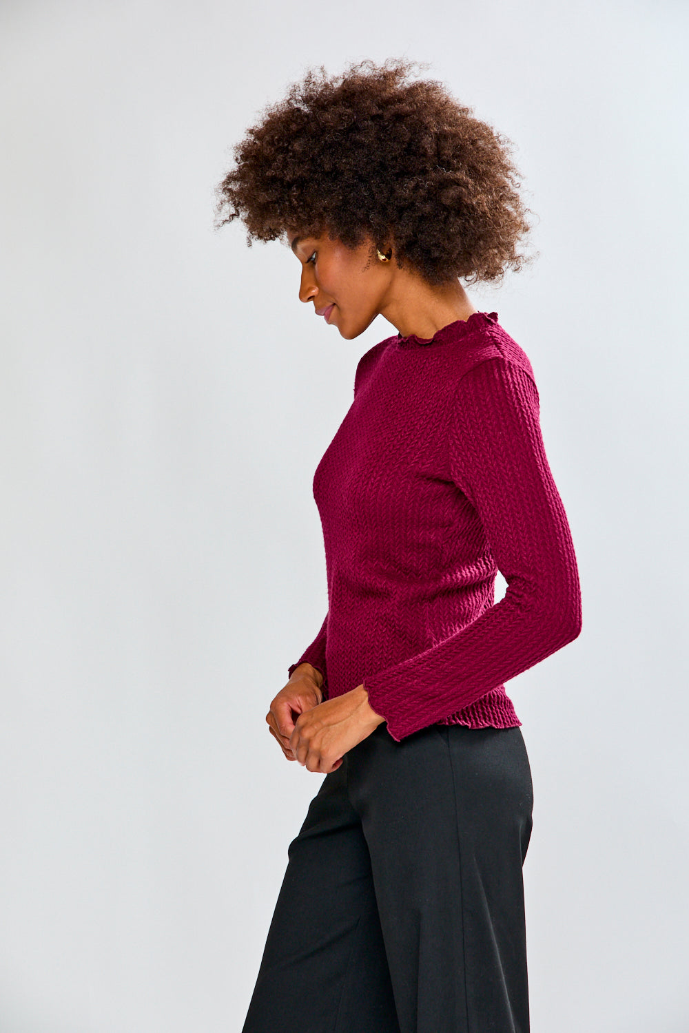 Woman wearing a burgundy shirt and black pants against a white background