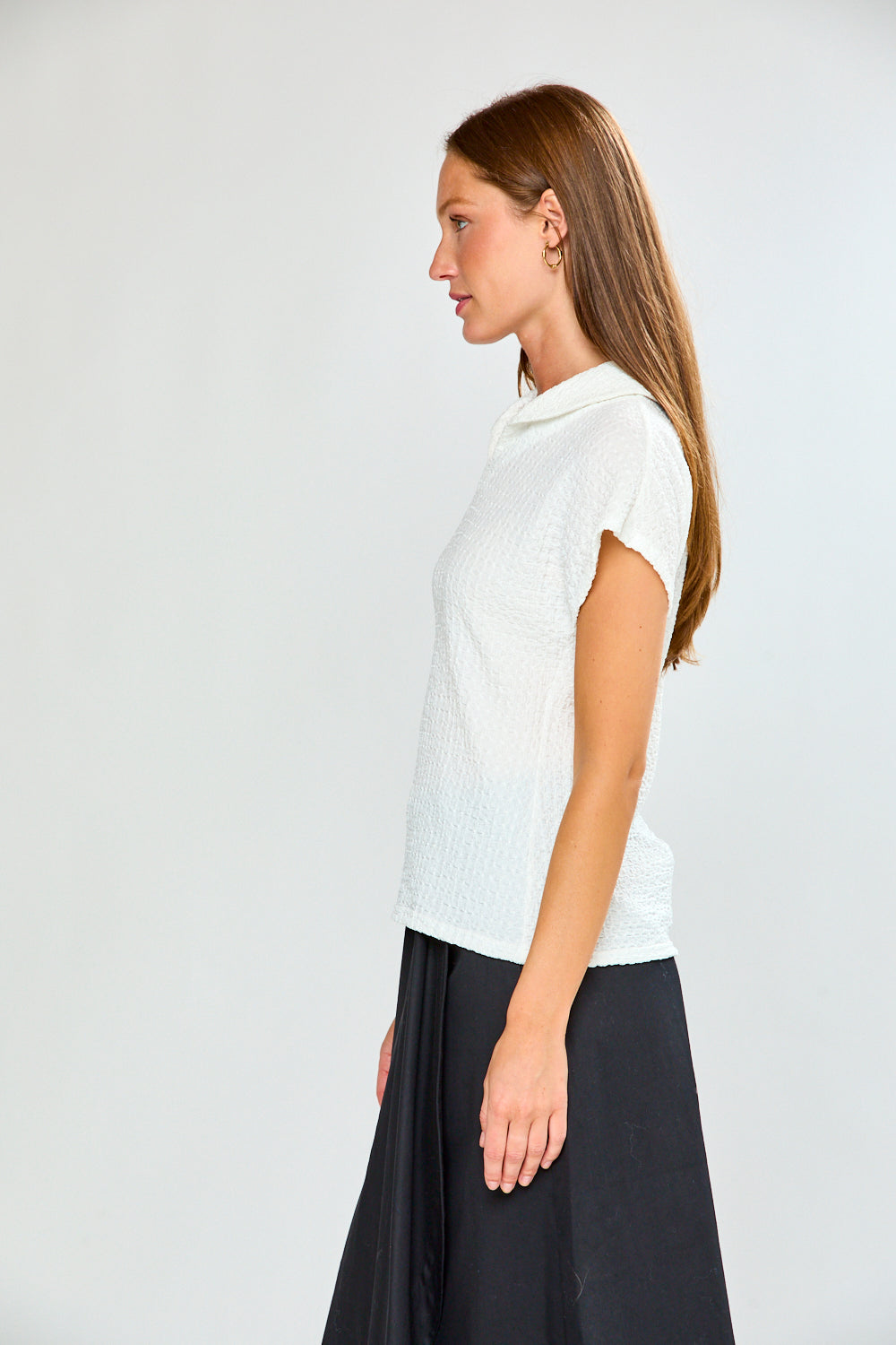 Woman wearing a white short-sleeve top and black skirt on a plain background