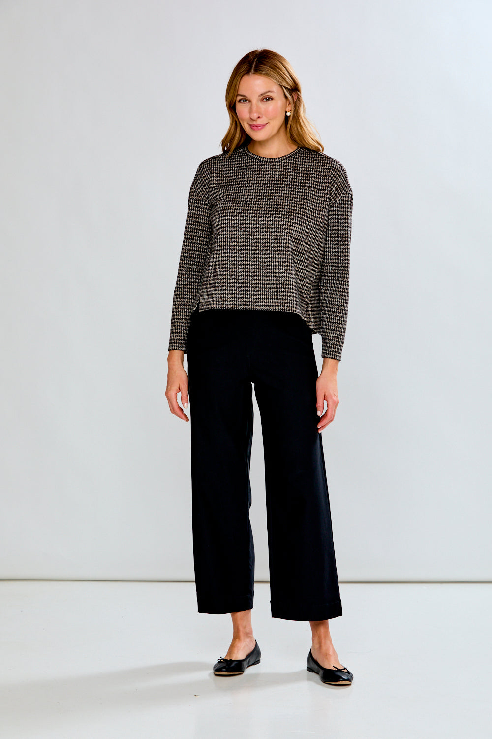 Woman wearing a plaid top with black pants on a light gray background