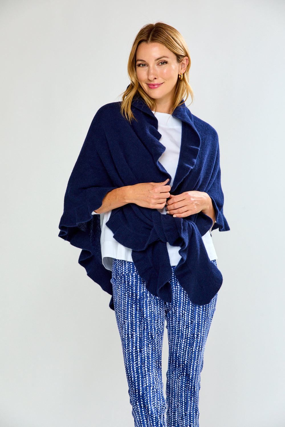 Woman wearing a navy blue ruffle triangle wrap over a white top and blue patterned pants on a white background