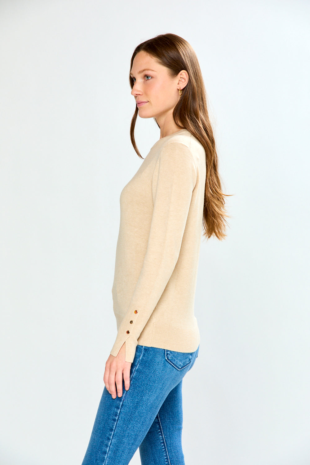 Woman wearing a sand sweater and blue jeans against a white background