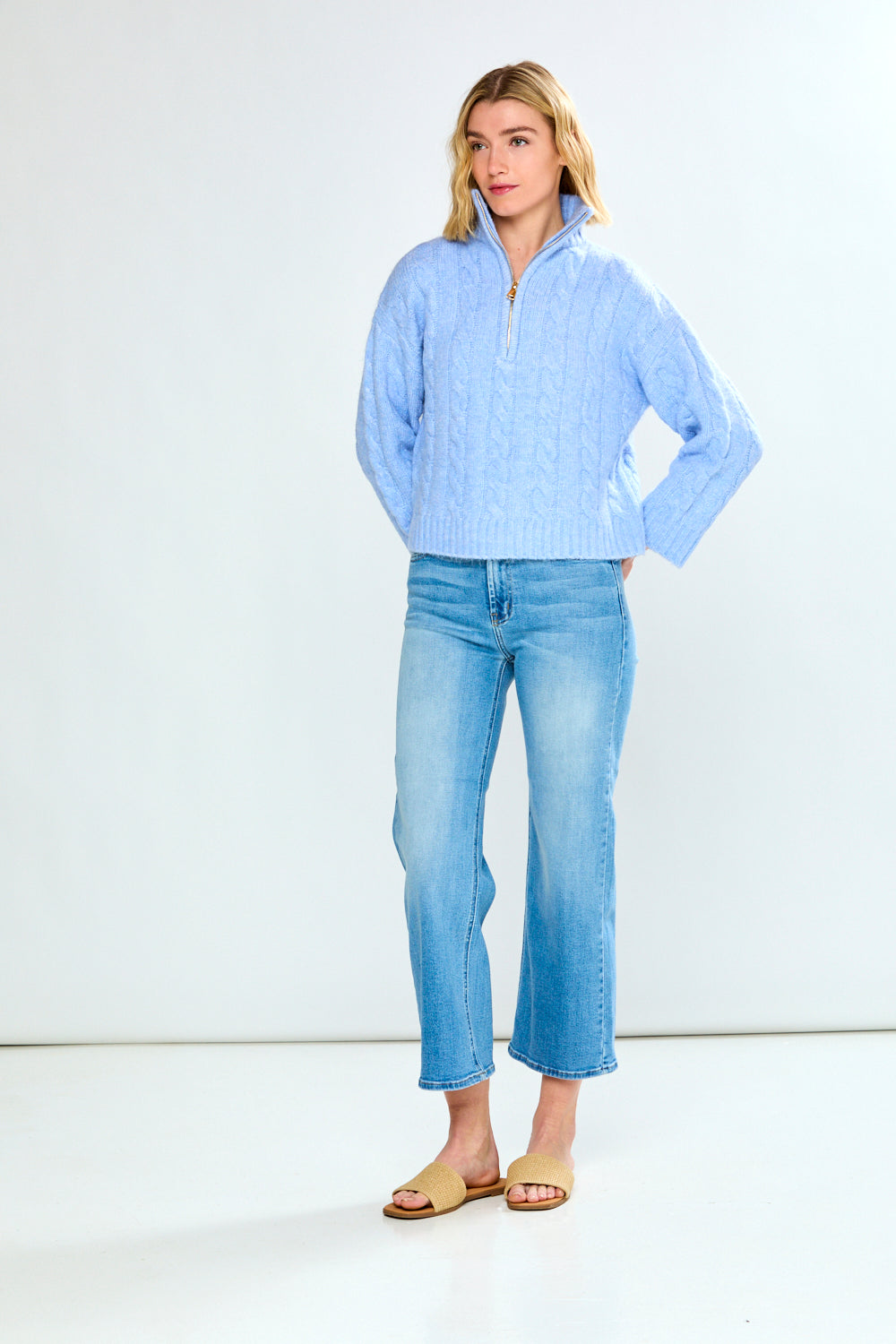 Woman wearing a denim cable knit sweater and blue jeans on a white background