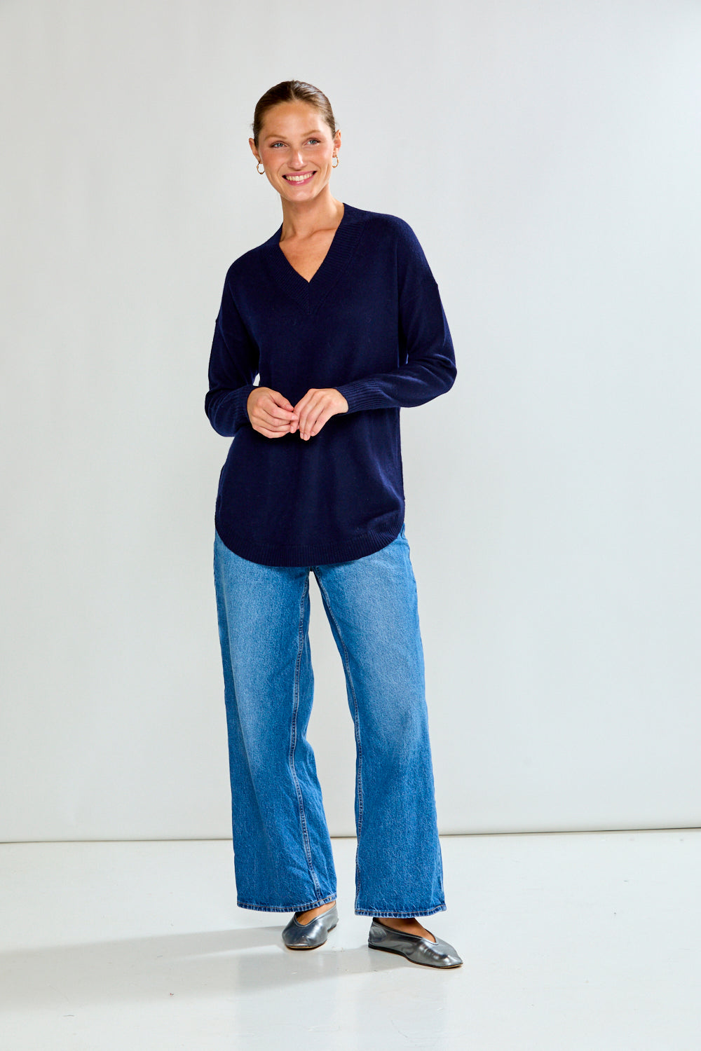 Woman wearing a navy sweater and blue jeans against a plain background