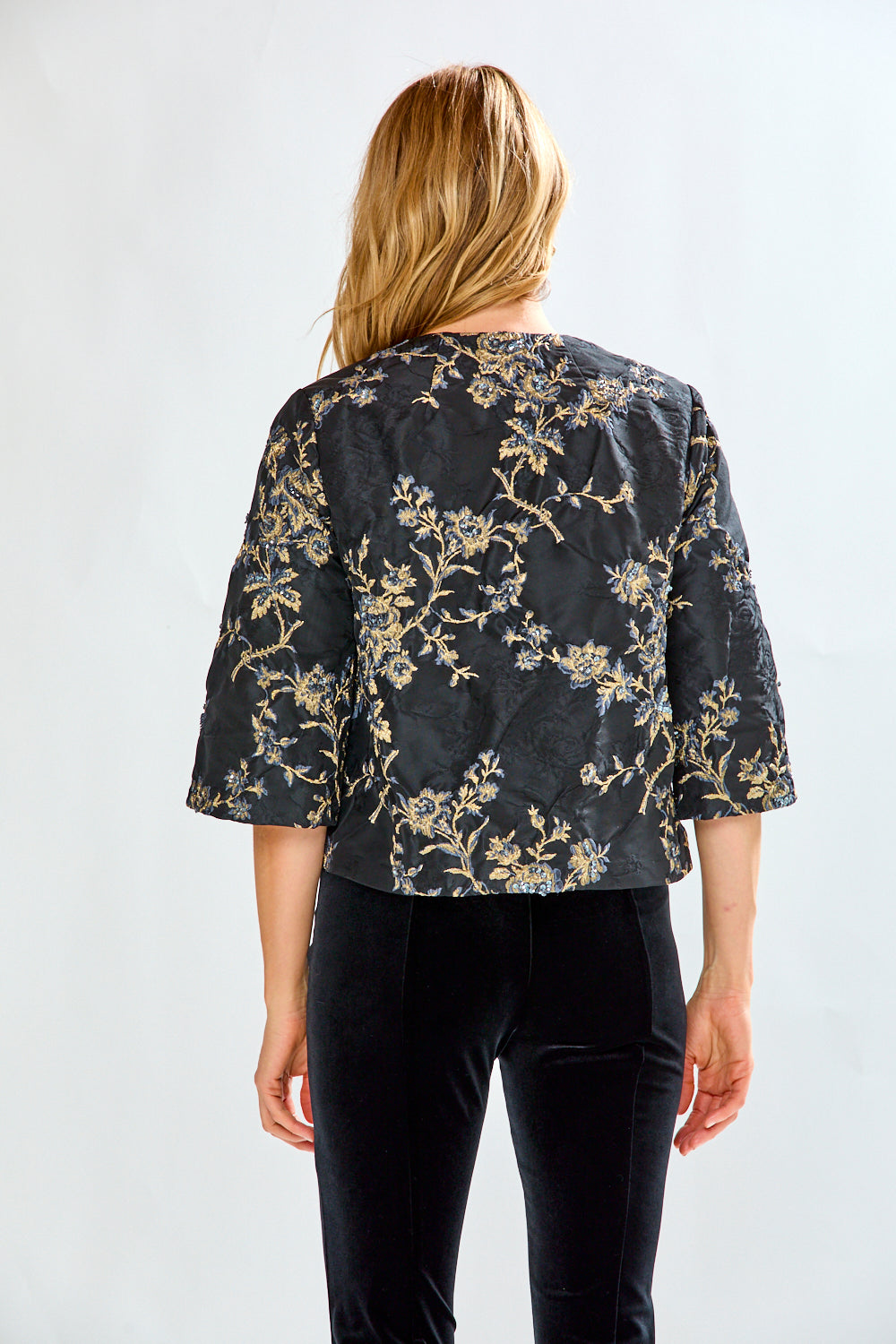 Woman wearing a black floral jacket and black pants on a white background