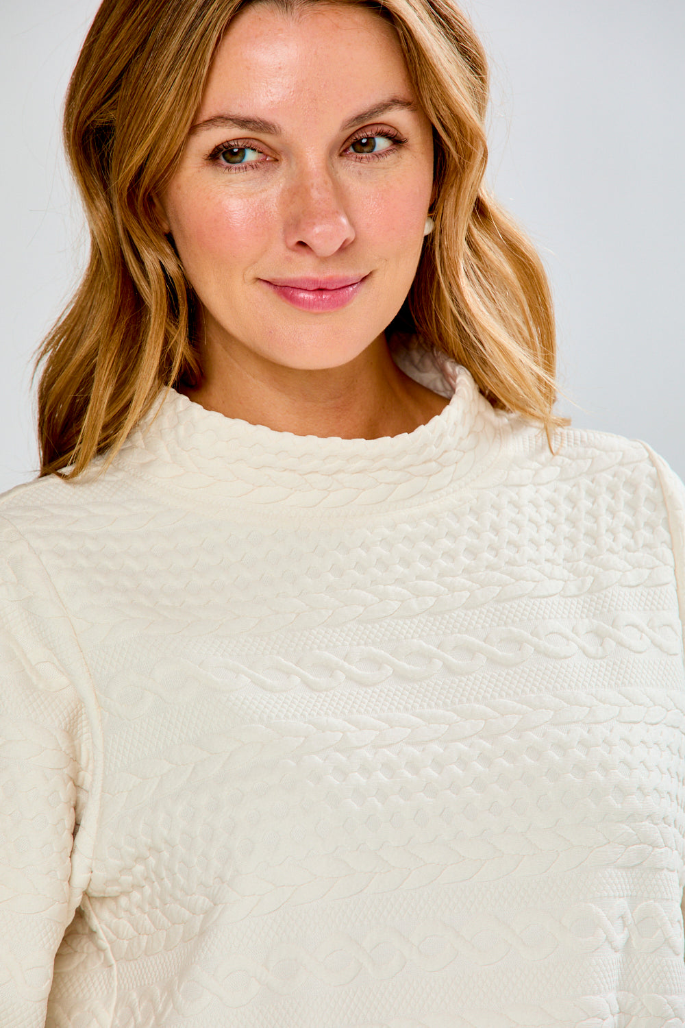 Woman wearing a cream sweater and plaid pants against a white background