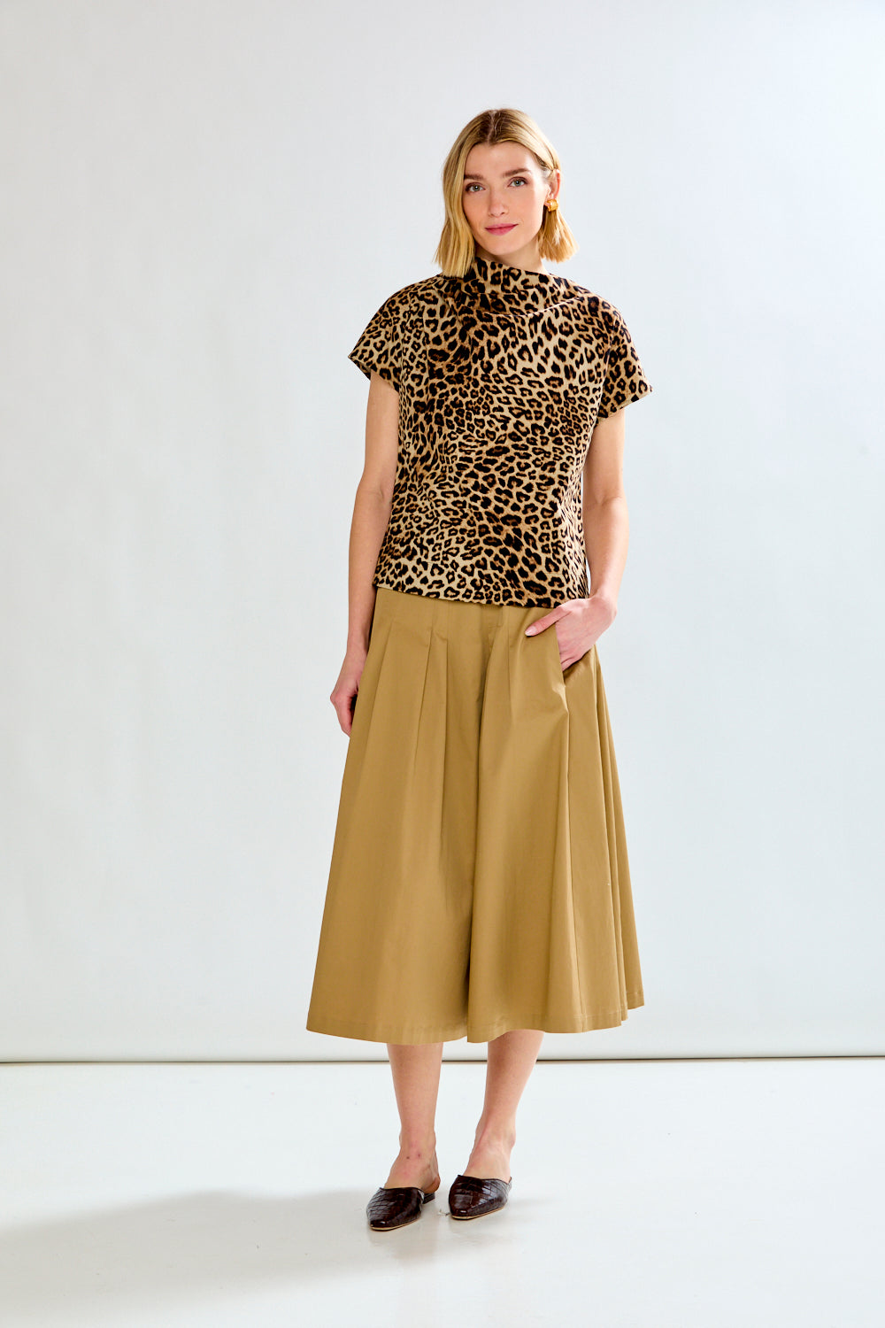 Woman wearing a leopard print top and beige skirt on a white background