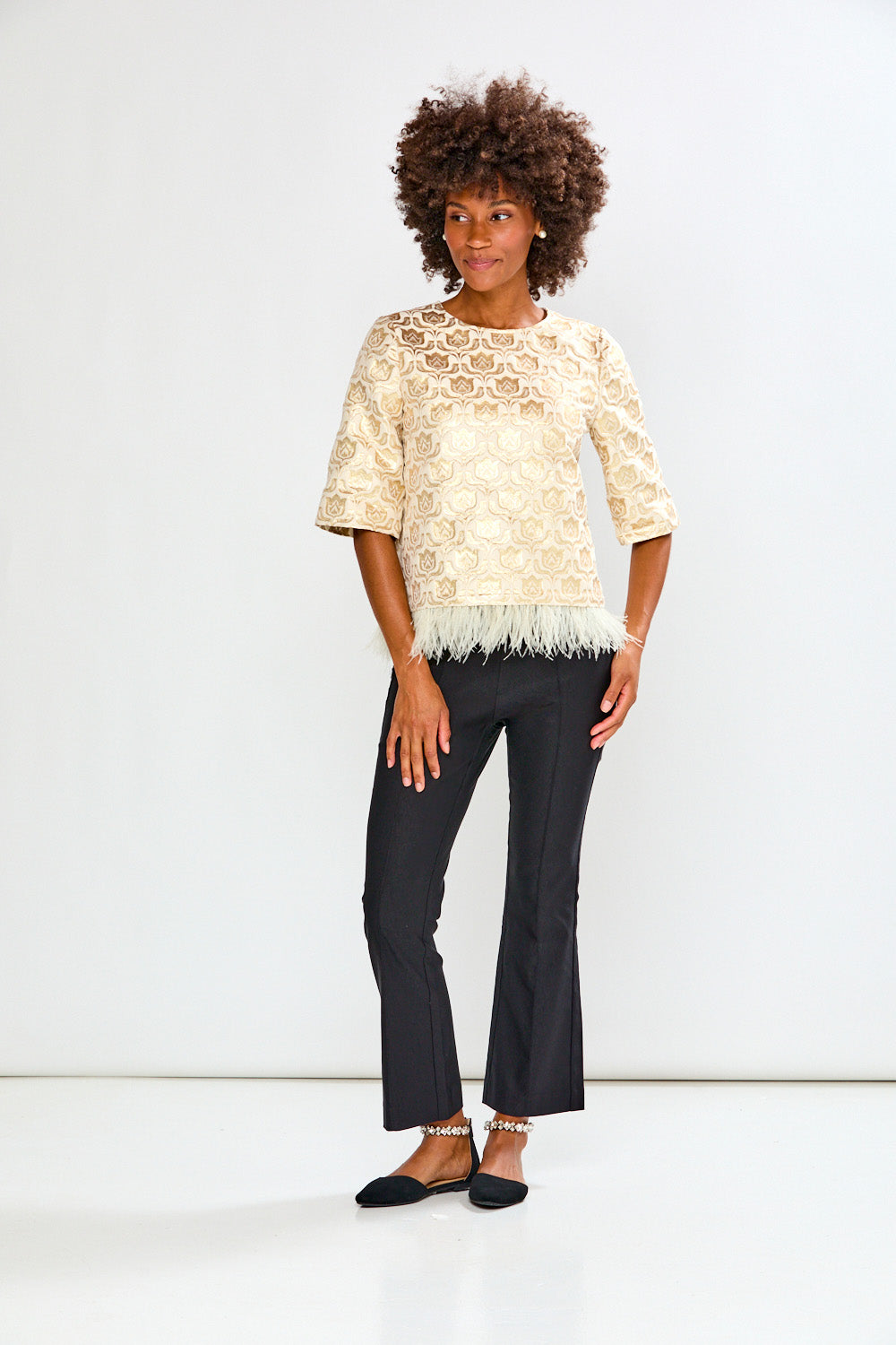 Woman wearing a beige lace top and black pants against a white background