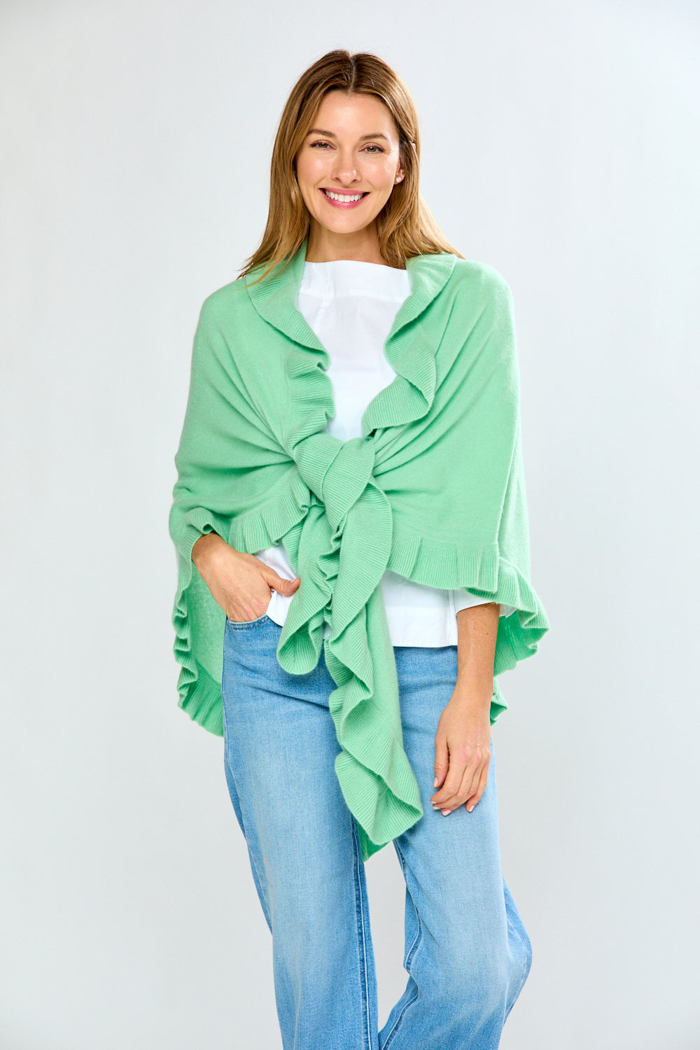 Woman wearing a light green wrap over a white top and blue jeans on a plain background