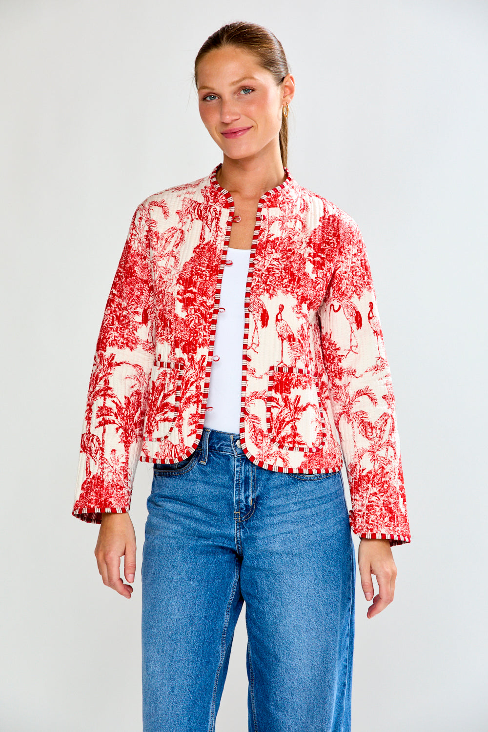 Woman wearing a red and white floral jacket with blue jeans on a white background