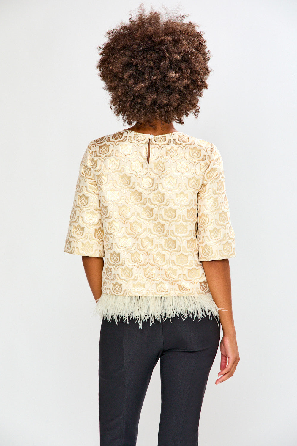 Person wearing a beige lace top with black pants on a white background