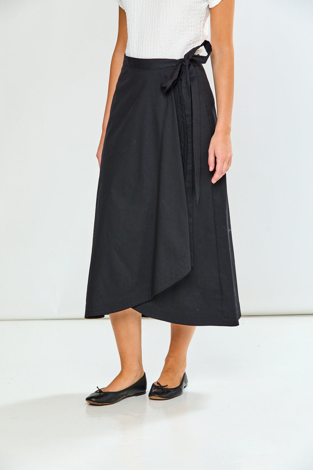 Person wearing a black wrap skirt with a white top on a white background