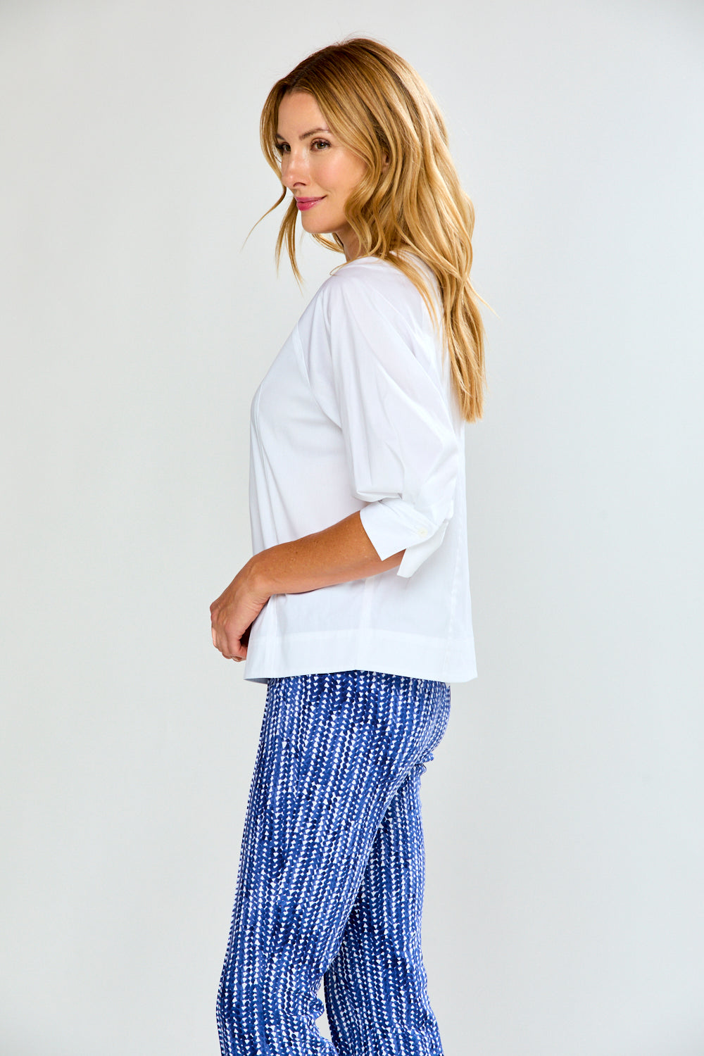 Woman wearing a white blouse and blue patterned pants on a plain background