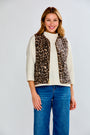 Woman wearing a leopard print vest over a white sweater and blue jeans on a light gray background