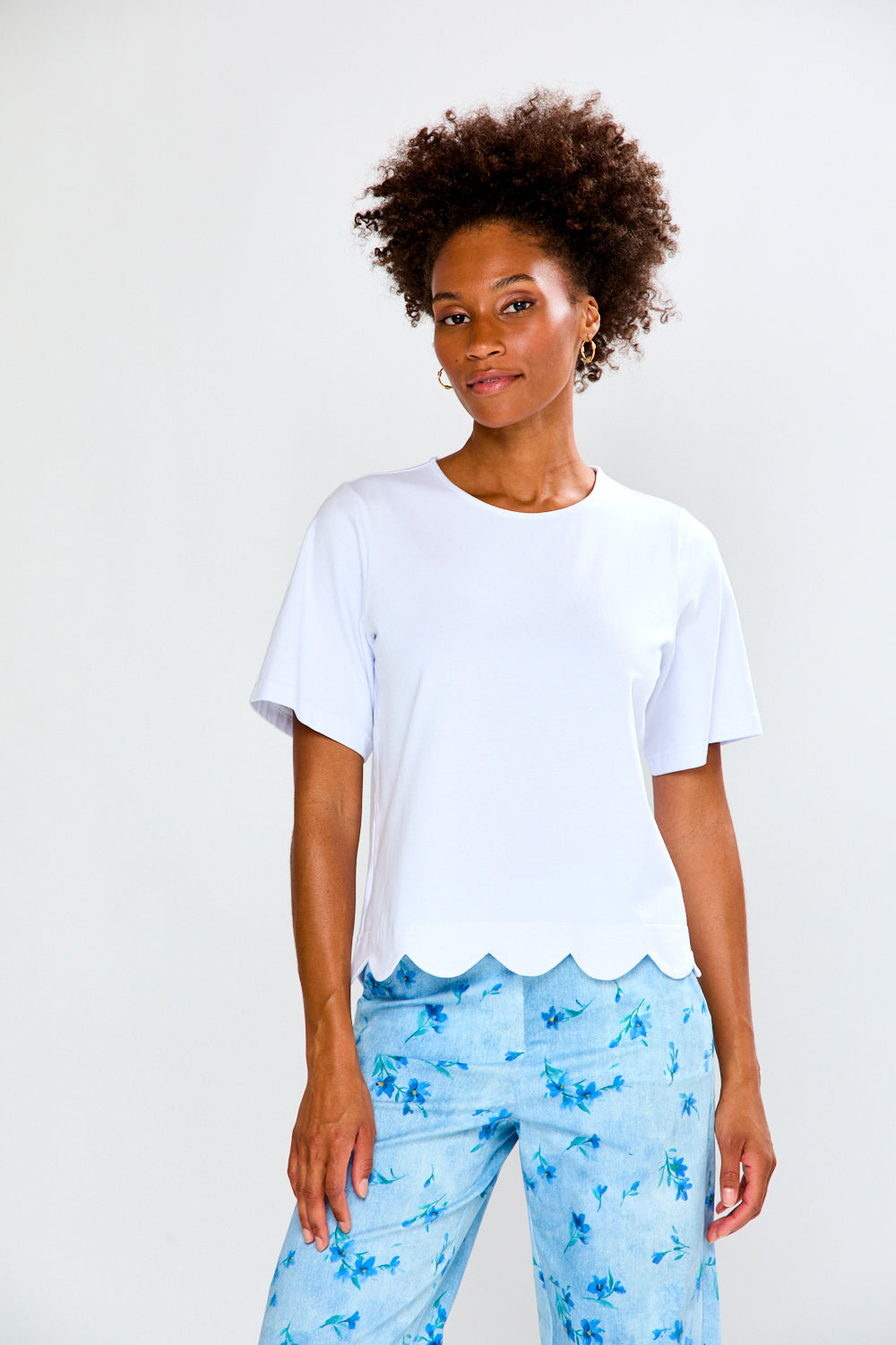 Woman wearing a white scalloped-edge top and light blue floral pants on a white background
