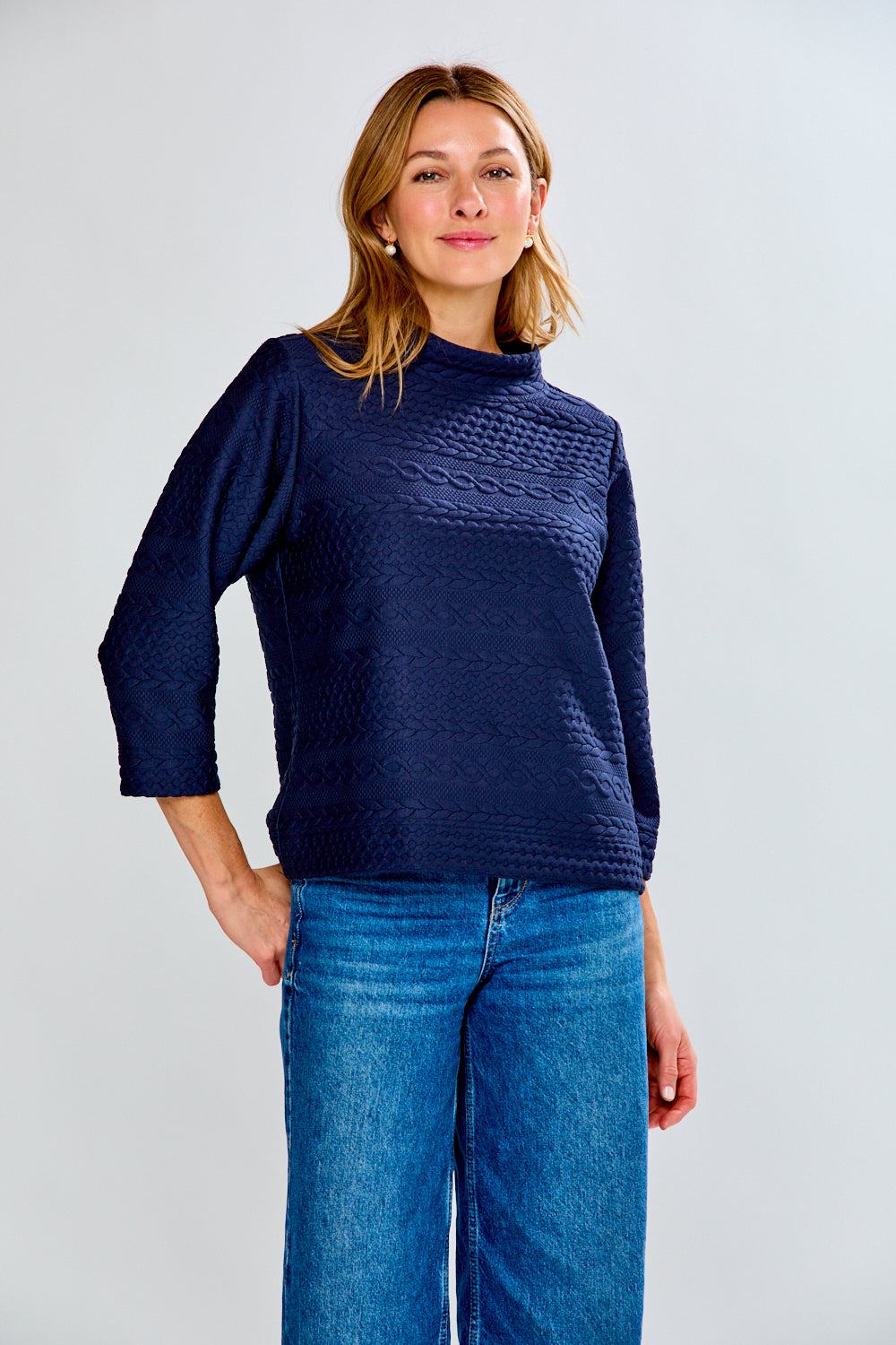 Woman wearing a navy blue textured sweater and blue jeans on a white background