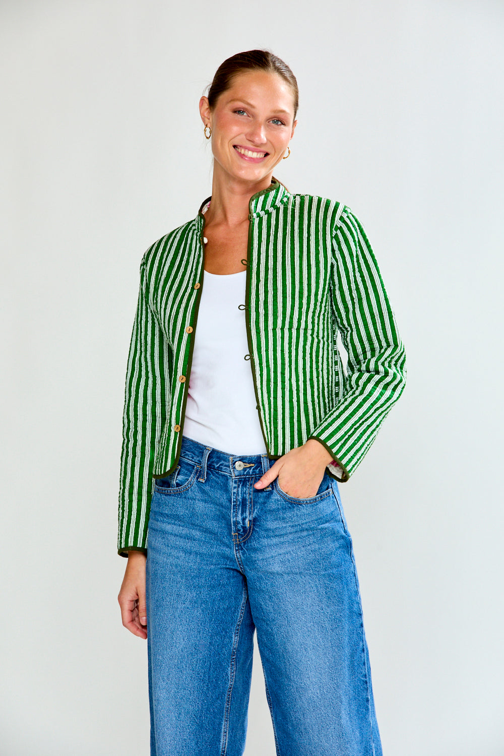 Woman wearing a green and white striped jacket and blue jeans on a plain background