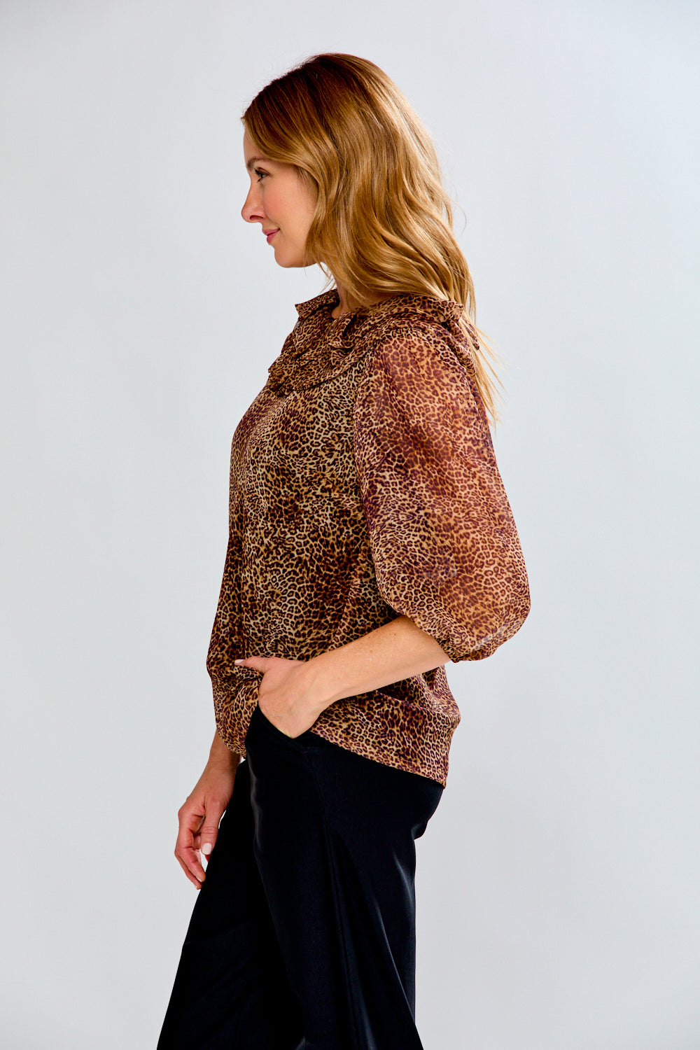 Woman wearing a patterned top and black pants on a white background