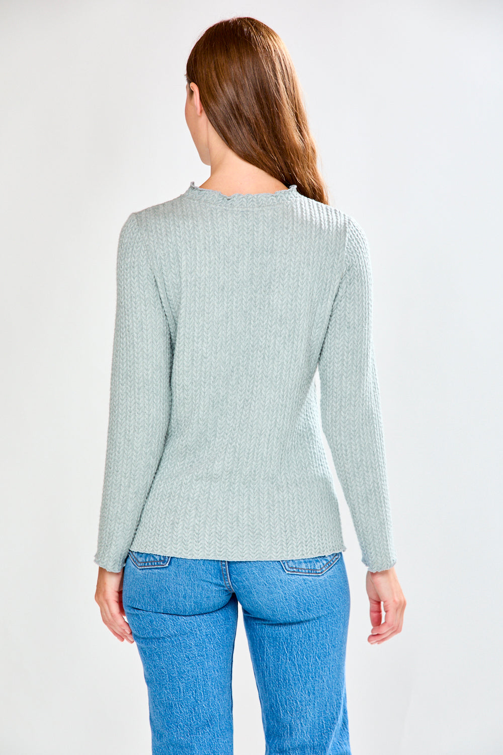 Woman wearing a light grey ribbed shirt and blue jeans on a white background