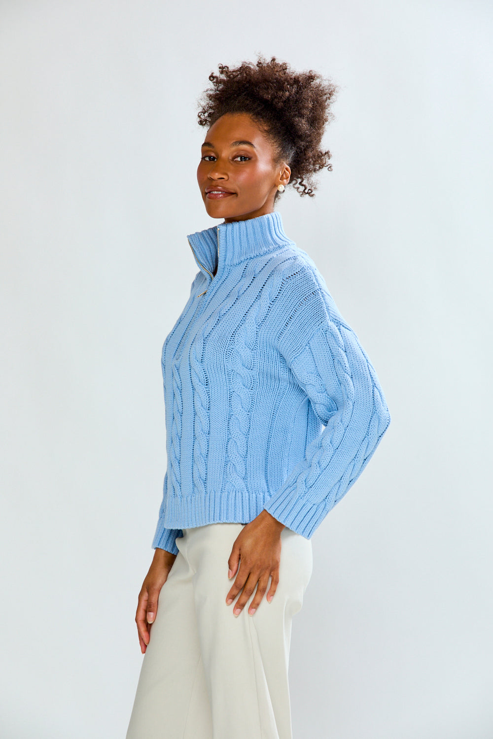 Woman wearing a light blue cable knit sweater against a white background
