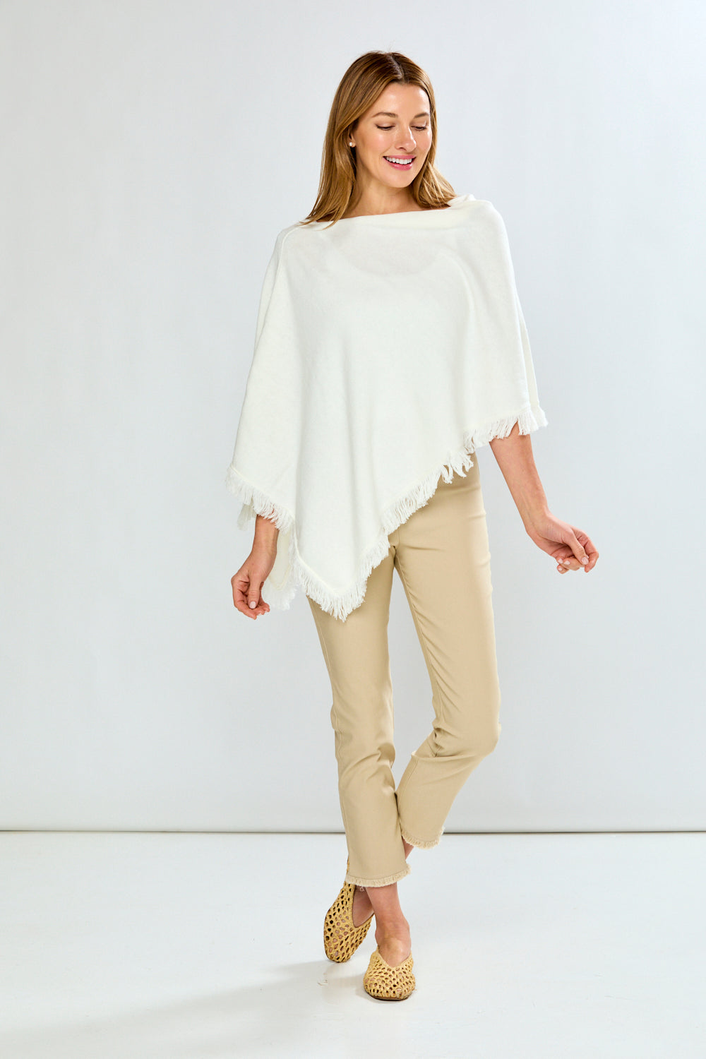 Woman wearing a white poncho and beige pants on a white background