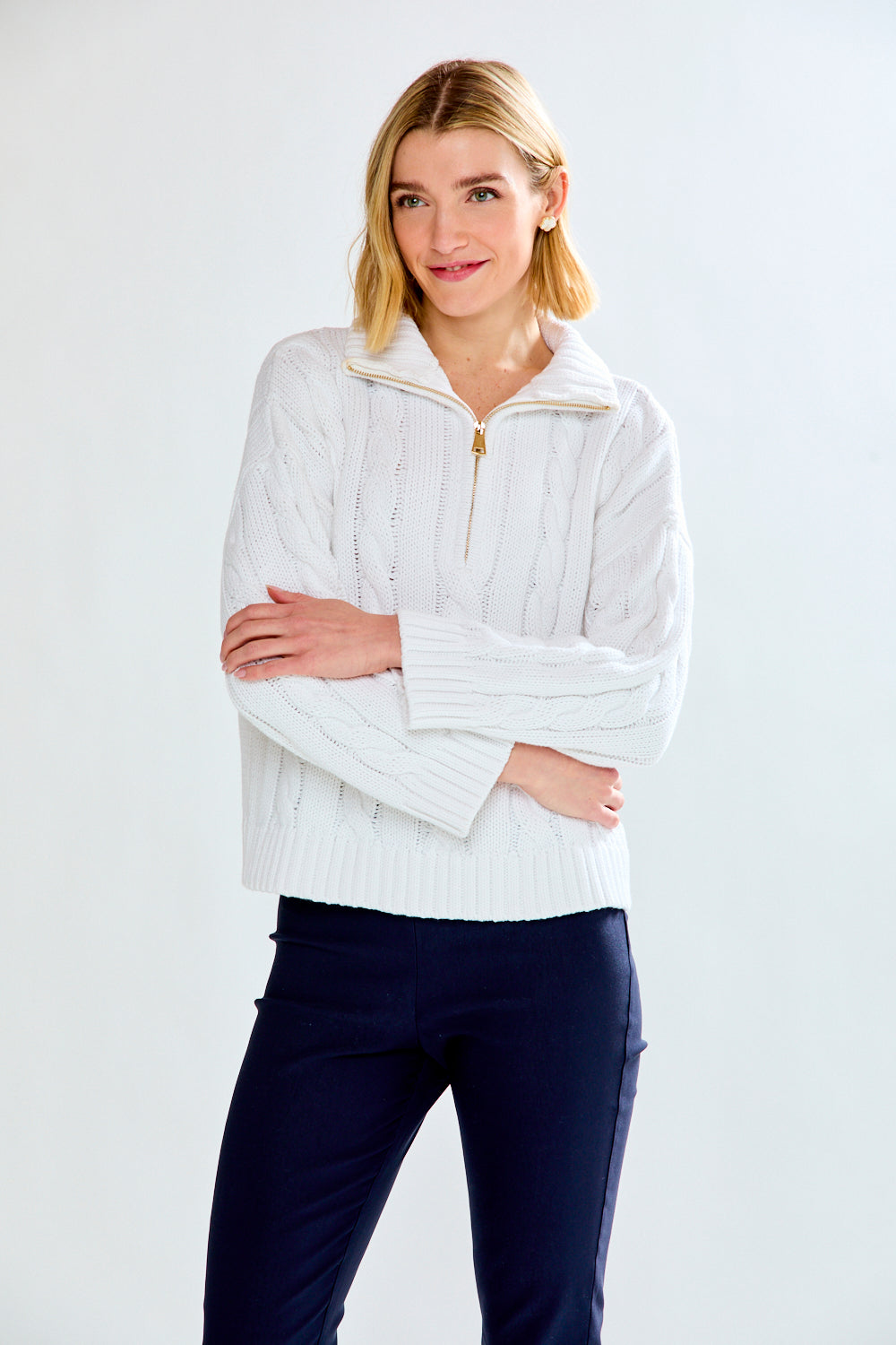 Woman wearing a white cable knit sweater against a plain background