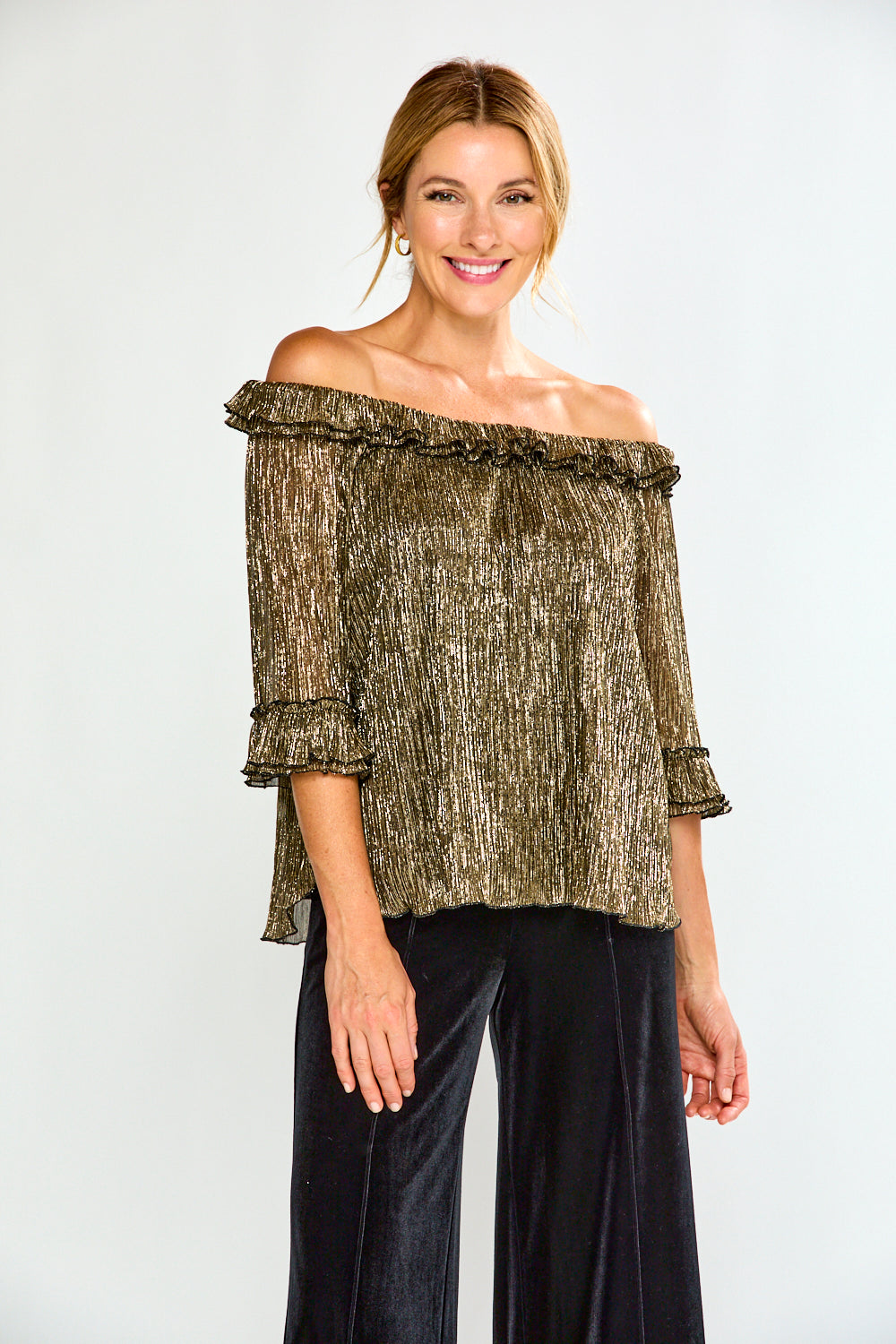 Woman wearing a gold off-shoulder top and black pants on a white background