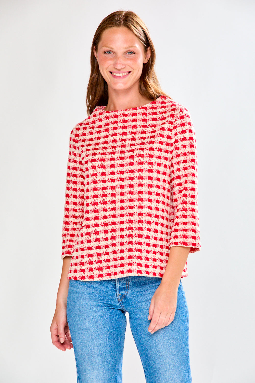 Woman wearing a red and white checkered shirt with blue jeans on a white background