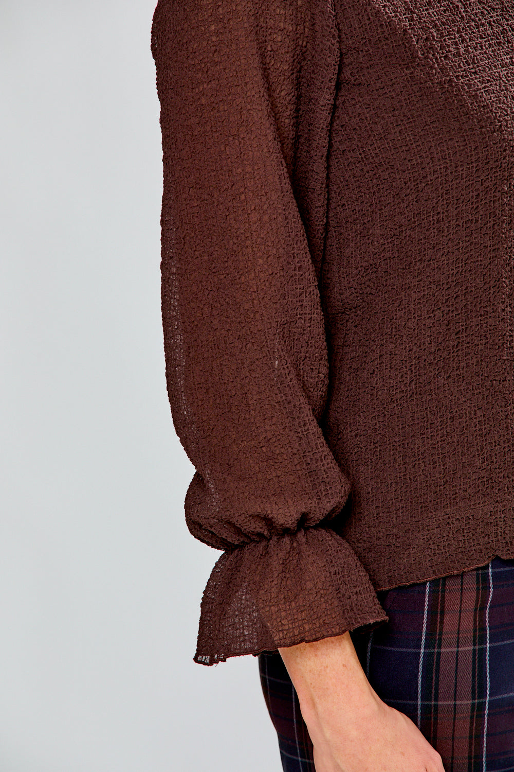 Brown textured blouse with plaid pants on a light gray background