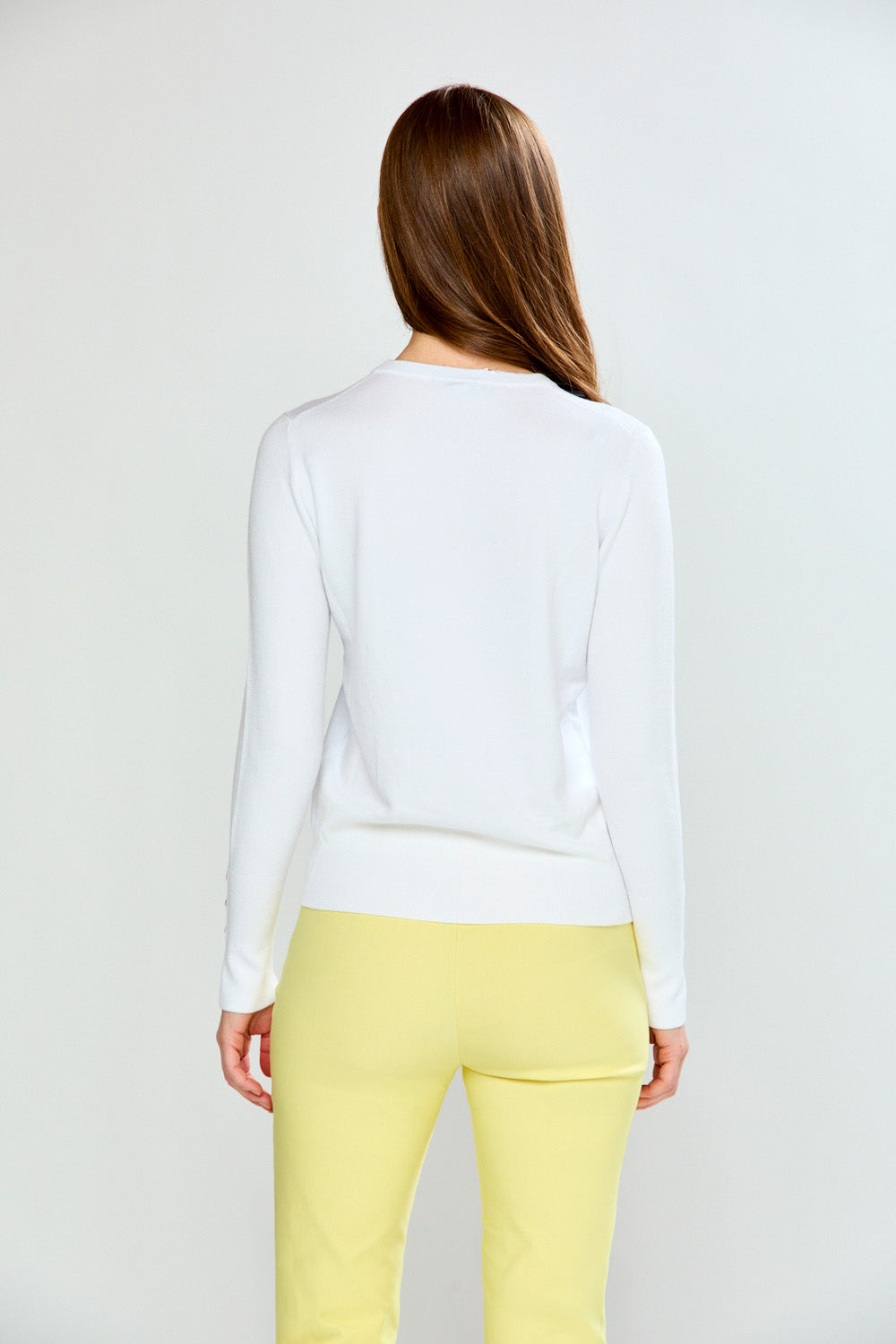 Woman wearing a white long-sleeve sweater and yellow pants on a light gray background