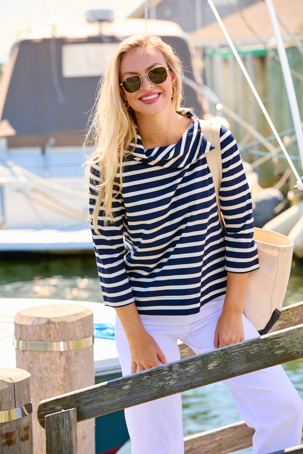 Woman wearing a striped shirt and sunglasses by a dock with boats in the background