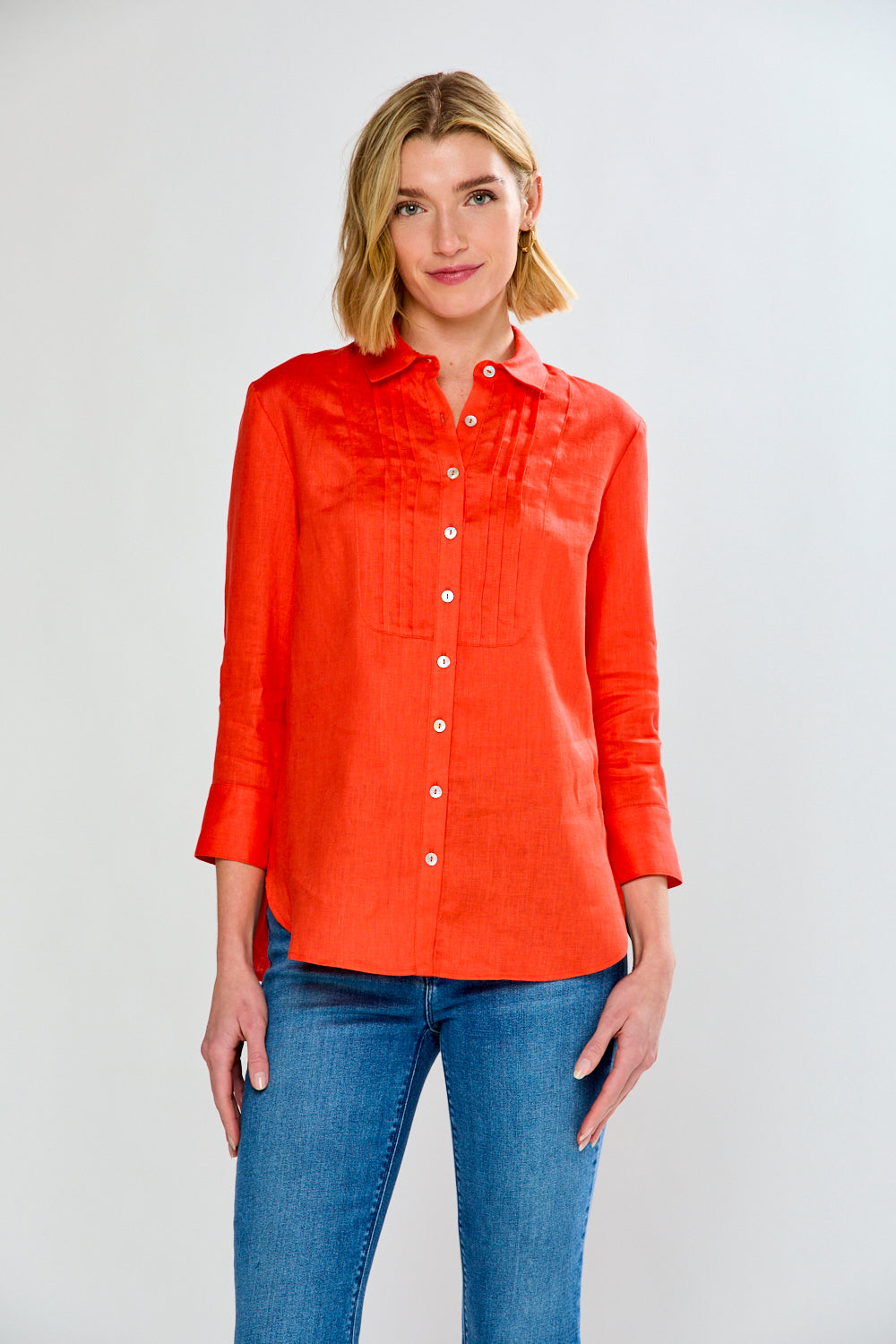 Woman wearing an orange button-up shirt and blue jeans on a white background
