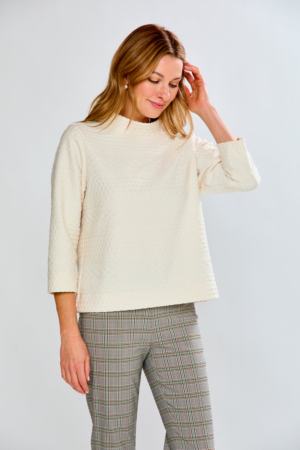 Woman wearing a cream sweater and plaid pants against a white background