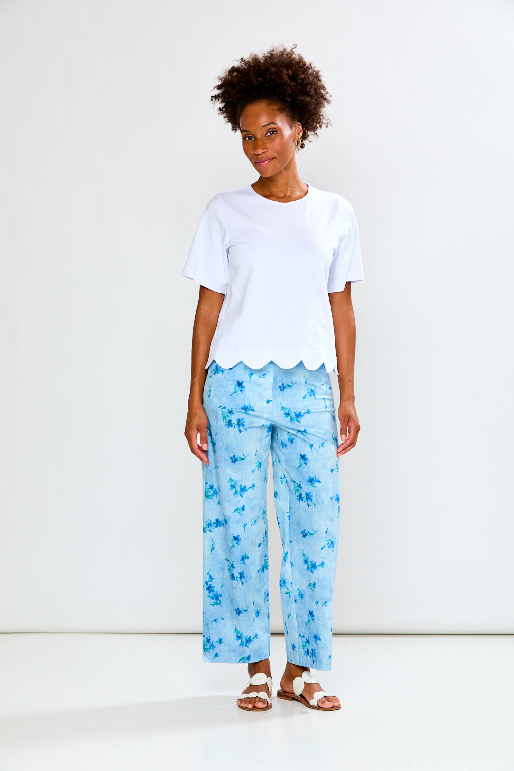 Woman wearing a white top and light blue floral pants on a white background