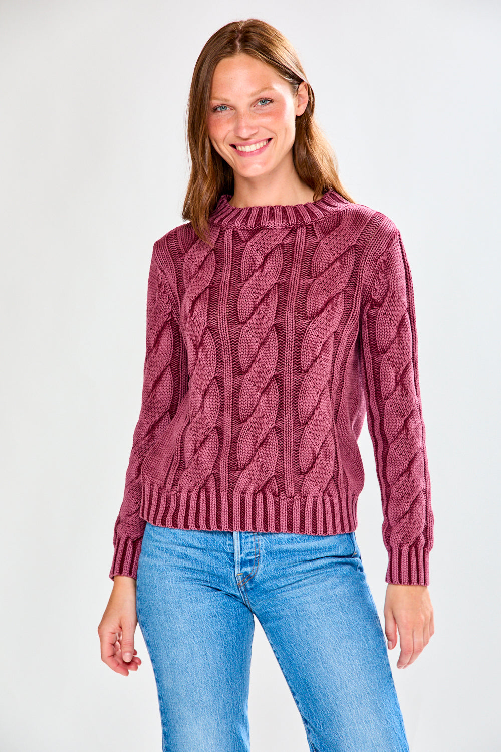 Woman wearing a raisin cable knit sweater and blue jeans on a white background