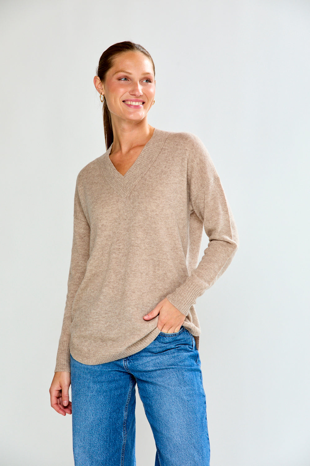 Woman wearing a beige sweater and blue jeans against a white background