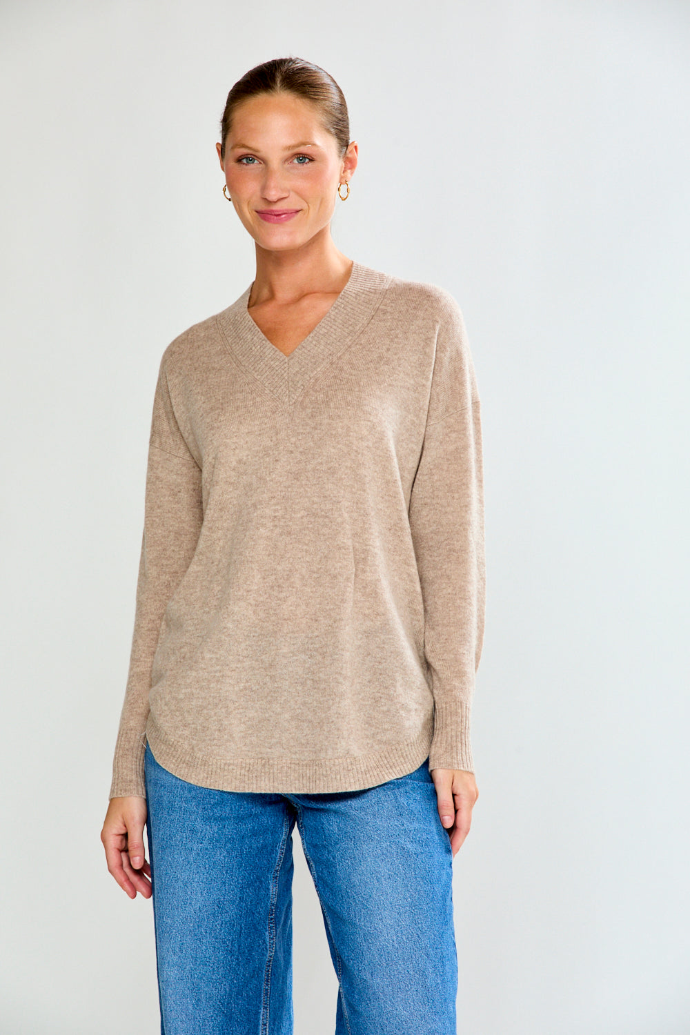 Woman wearing a beige sweater and blue jeans against a white background
