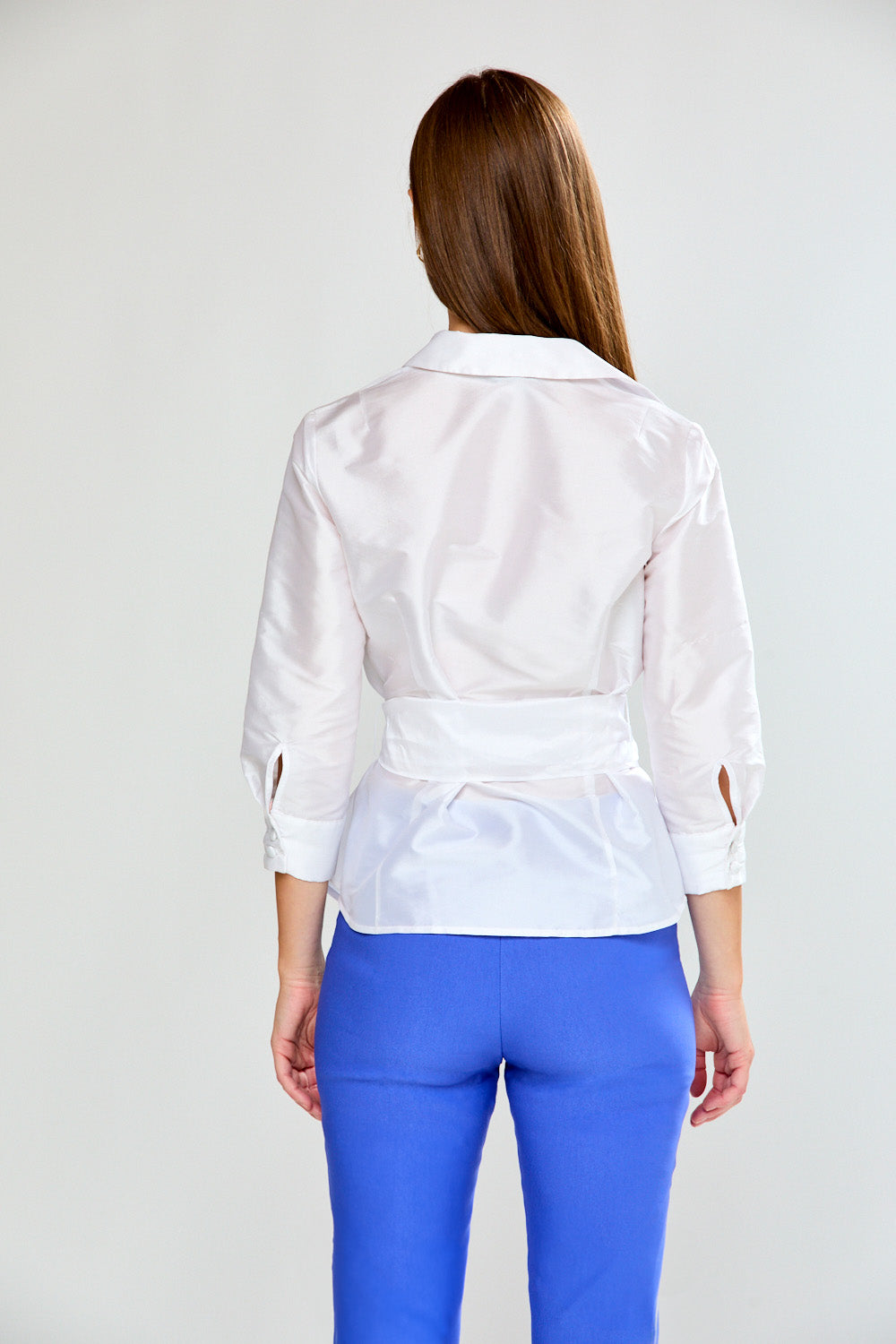 Woman wearing a white blouse with rolled-up sleeves and blue pants on a light gray background
