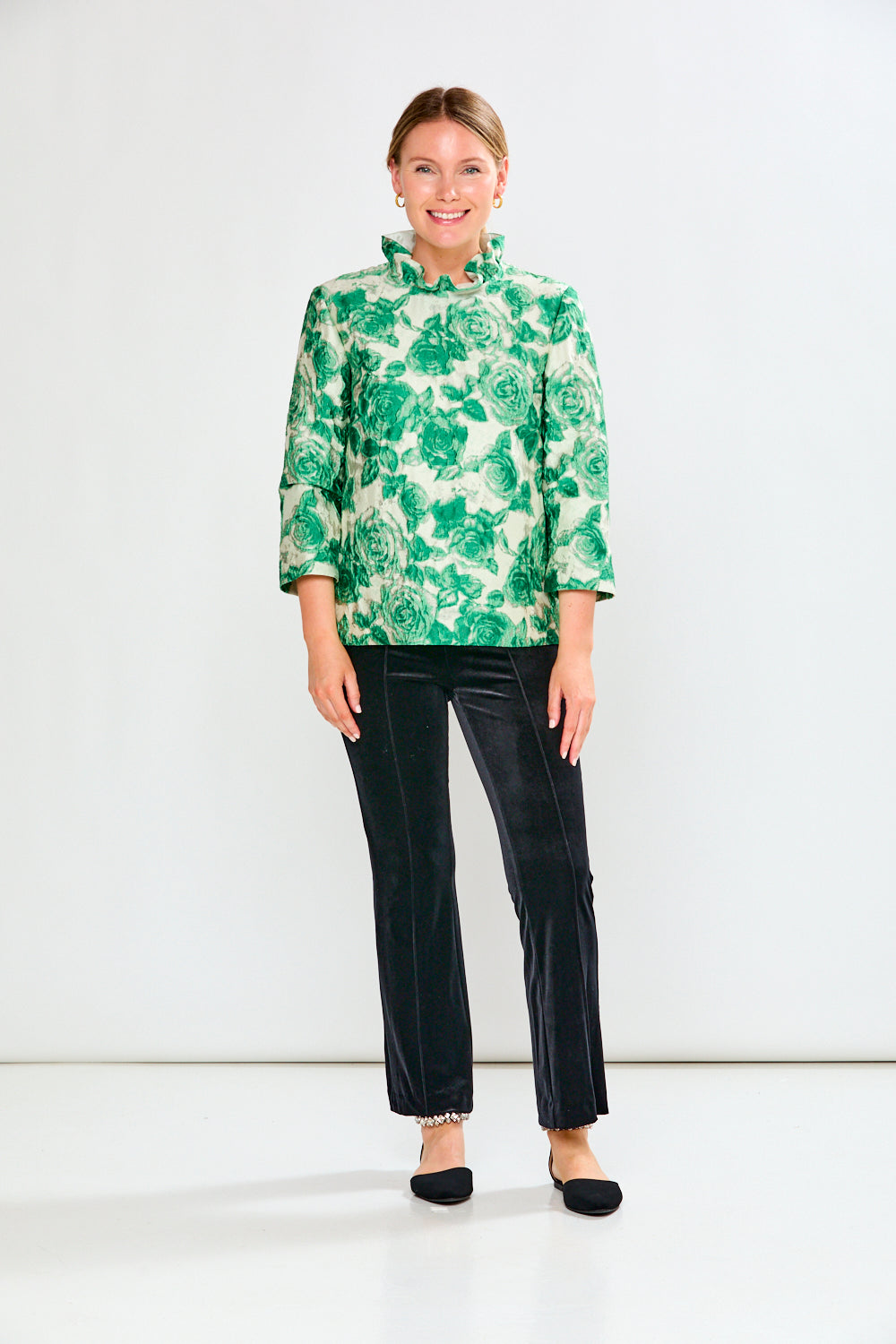 Woman wearing a green floral blouse and black pants on a white background