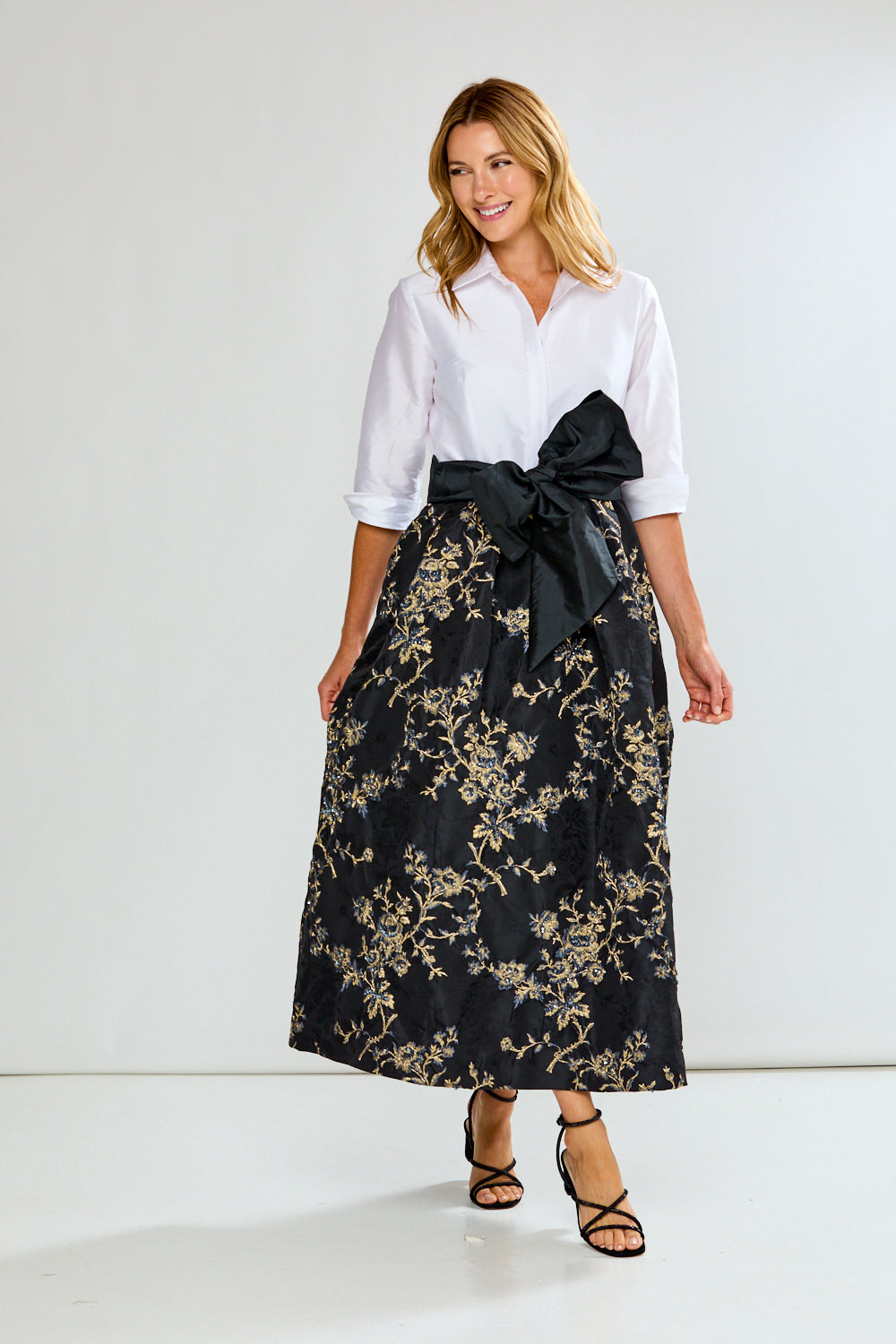 Woman wearing a dress with a white blouse and black floral skirt with a large bow on a white background
