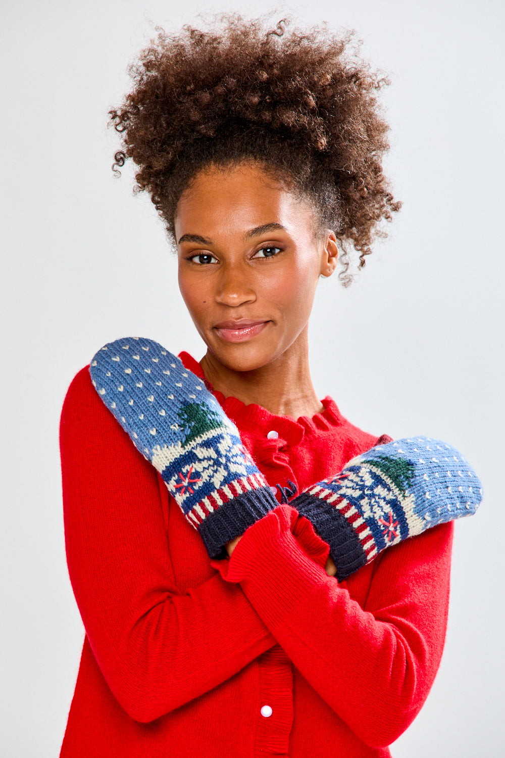 Woman wearing a red sweater and blue patterned mittens against a white background