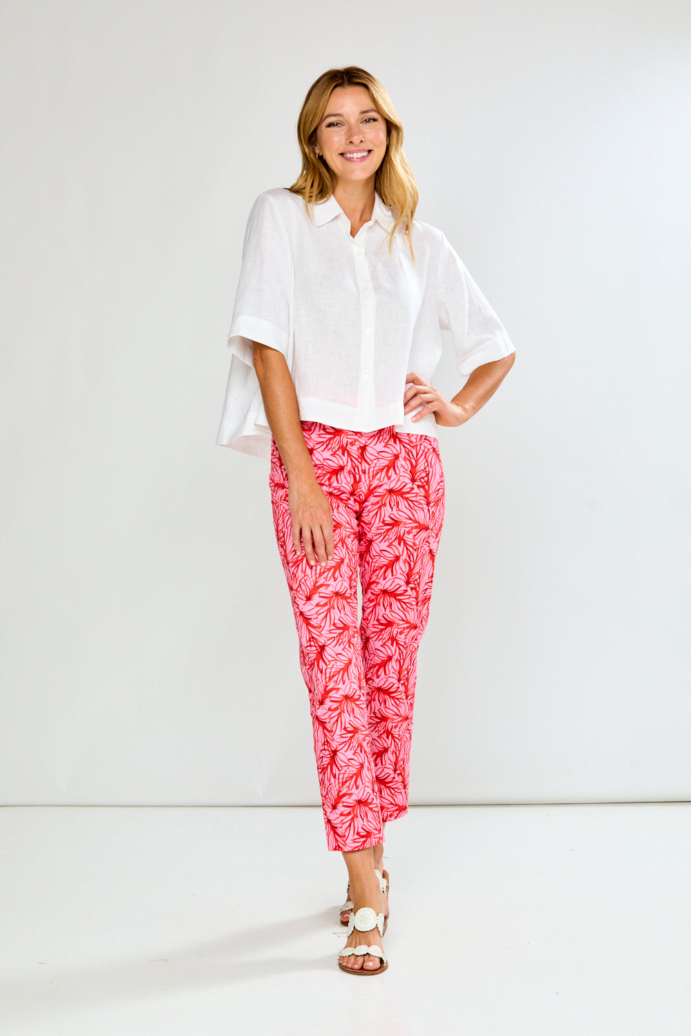 Woman wearing a white blouse and pink leaf-patterned pants on a white background