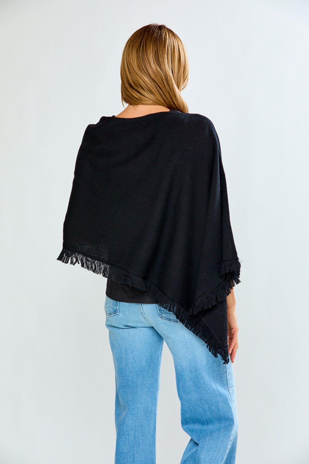 Person wearing a black poncho with frayed edges over a plain background