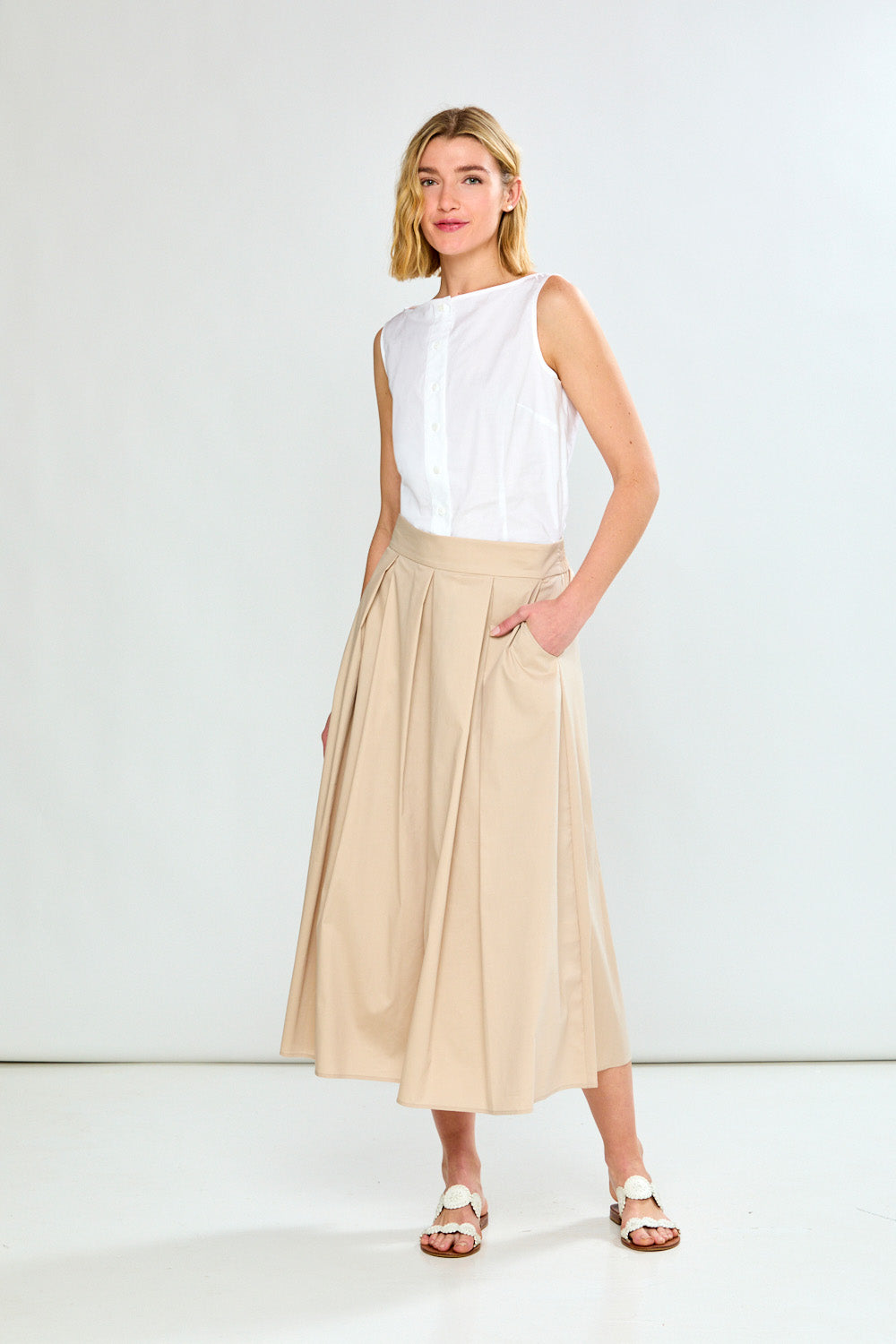 Woman wearing a white sleeveless top and beige skirt on a white background