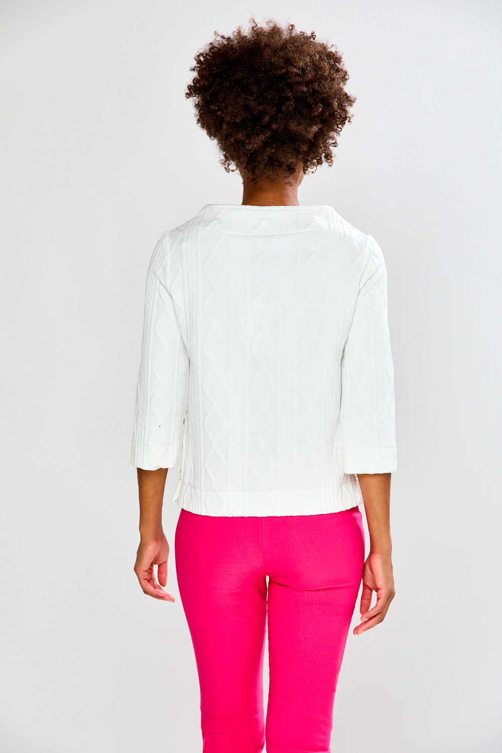 Woman wearing a white top and pink pants on a plain background