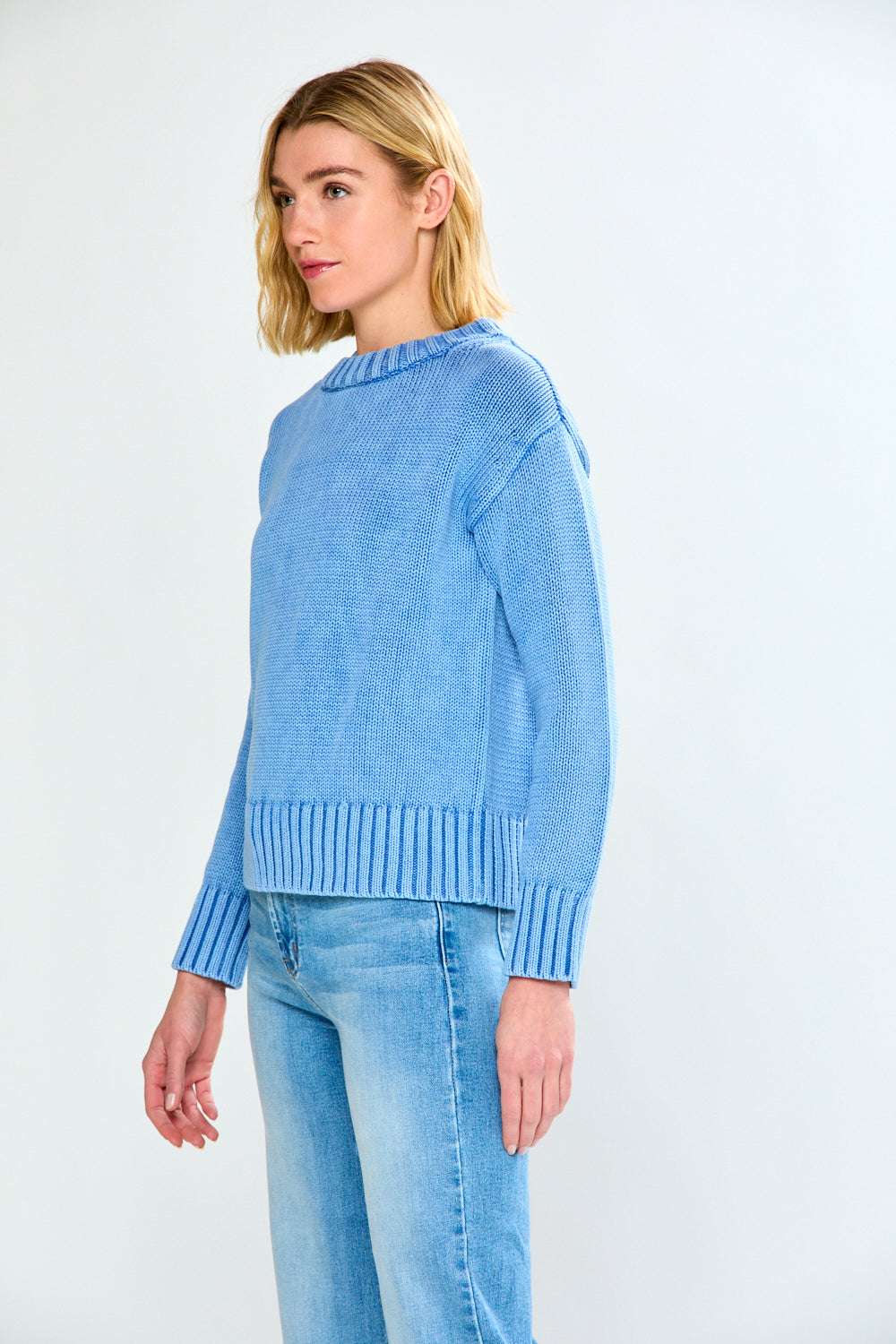 Woman wearing a blue sweater and light blue jeans on a white background