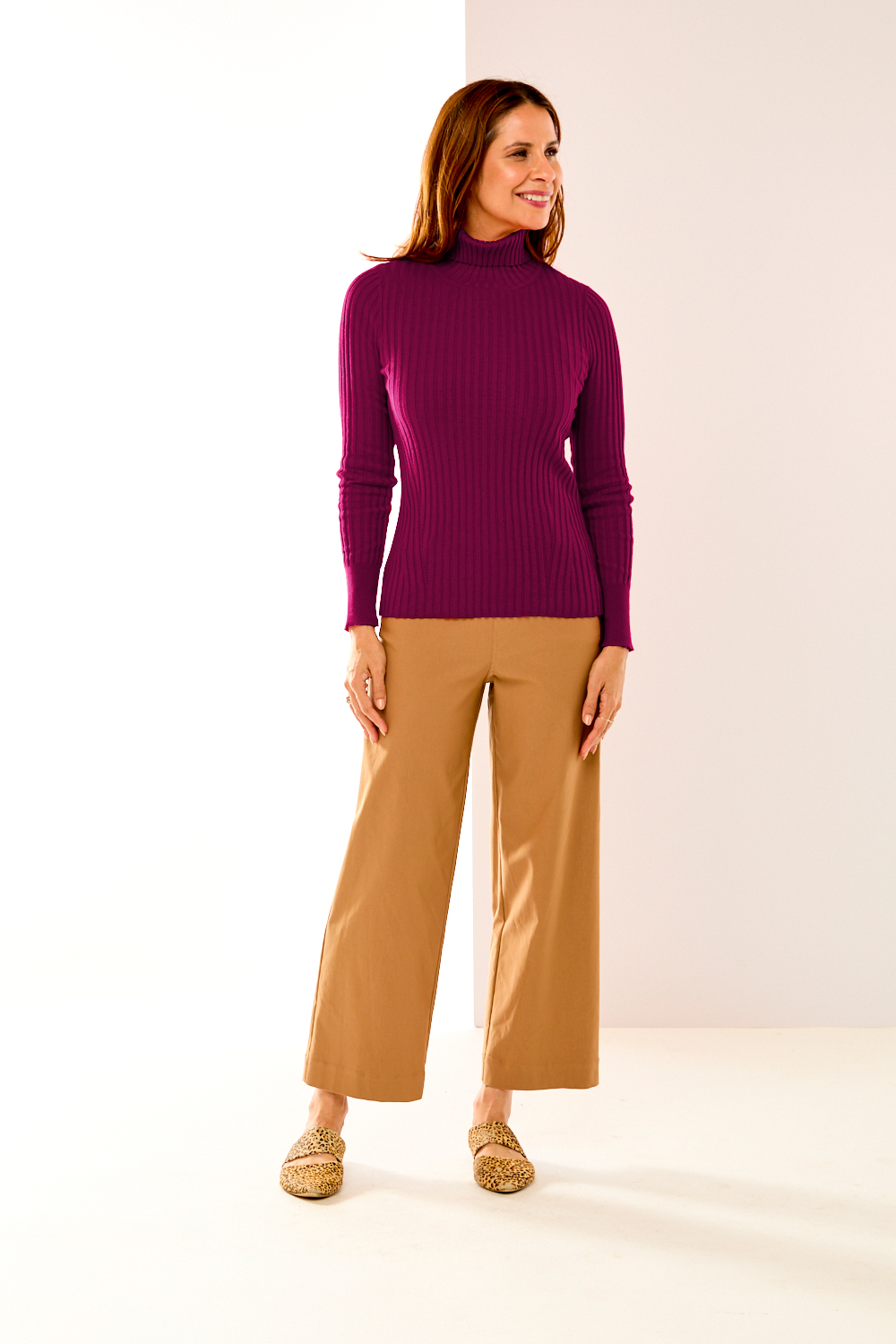 Woman wearing a purple turtleneck and beige pants on a white background
